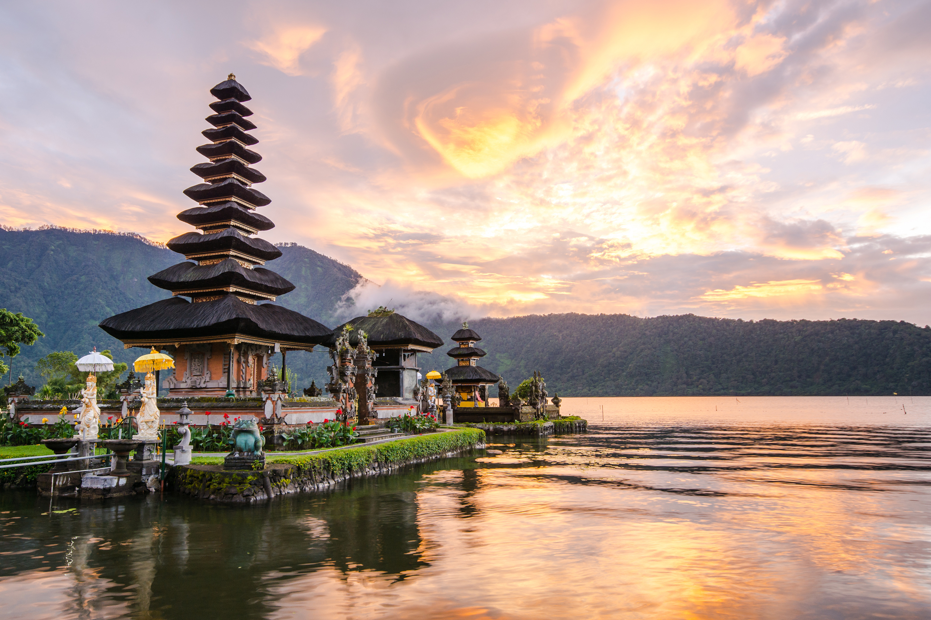 A Balinese temple with a stacked roof overlooks the water as the sunsets 