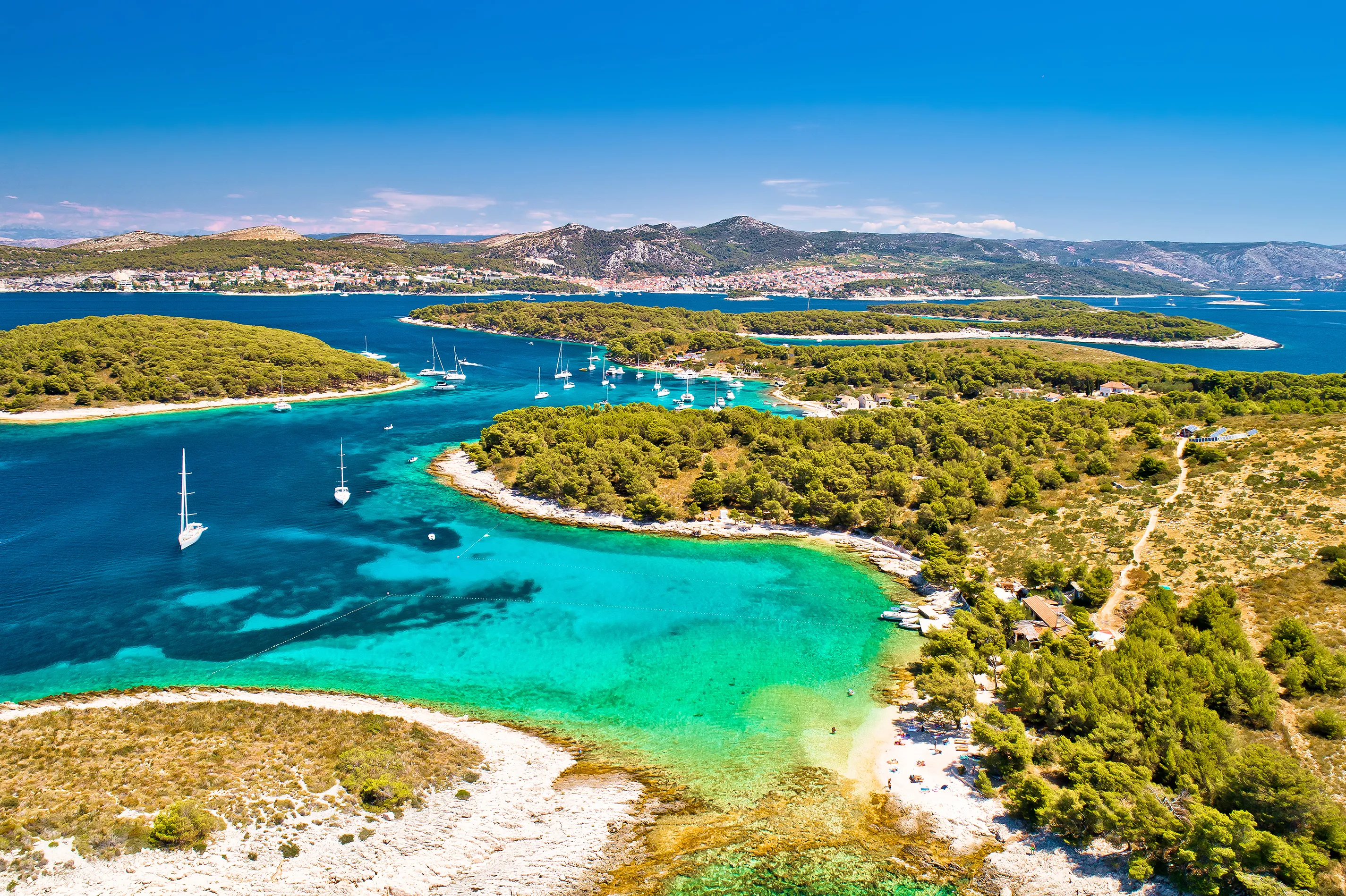 Verdant Mediterranean islands surrounded by turquoise water dotted with yachts with the mainland in the distance
