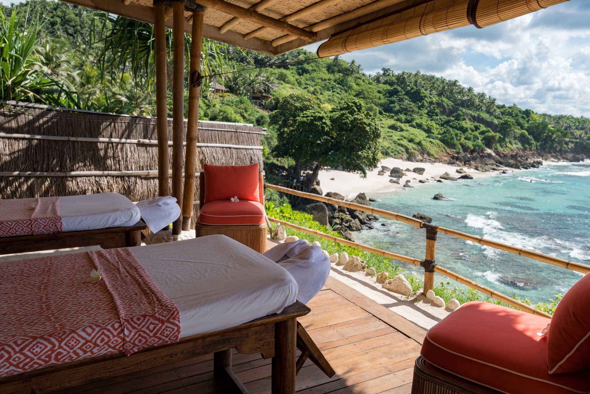 Open-air spa treatment area with massage beds overlooking a tropical coastline and clear blue sea.