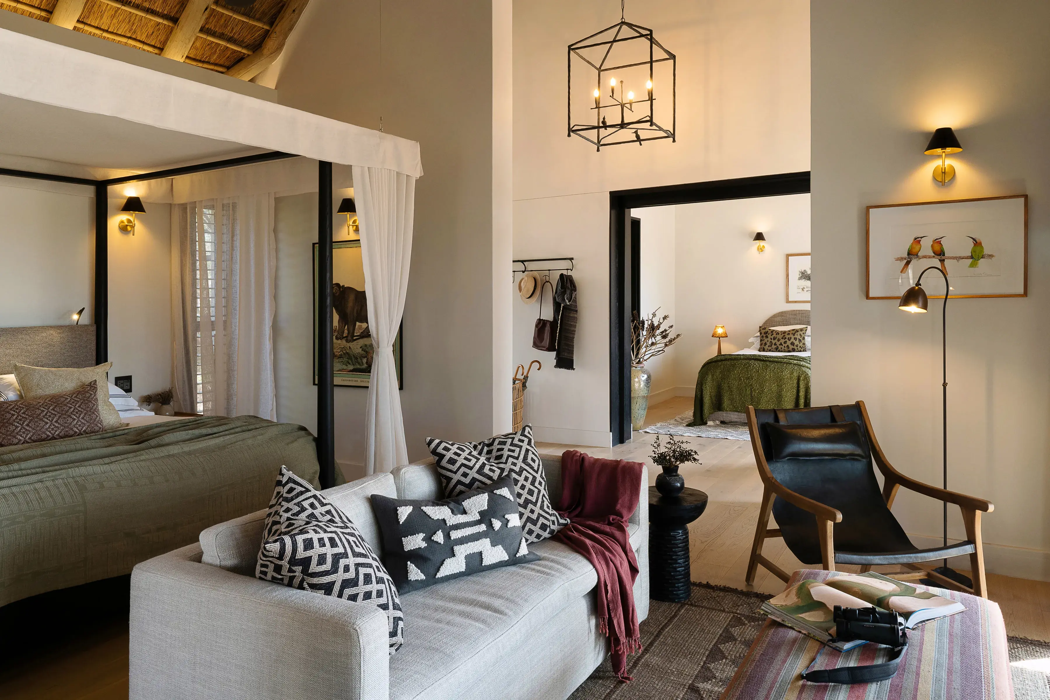 A family suite at Monwana Game Reserve featuring a comfy lounge area with sofa in front of a four posted bed with white mesh curtains, stylish Afro-modern decor and a glimpse of another room and bed behind