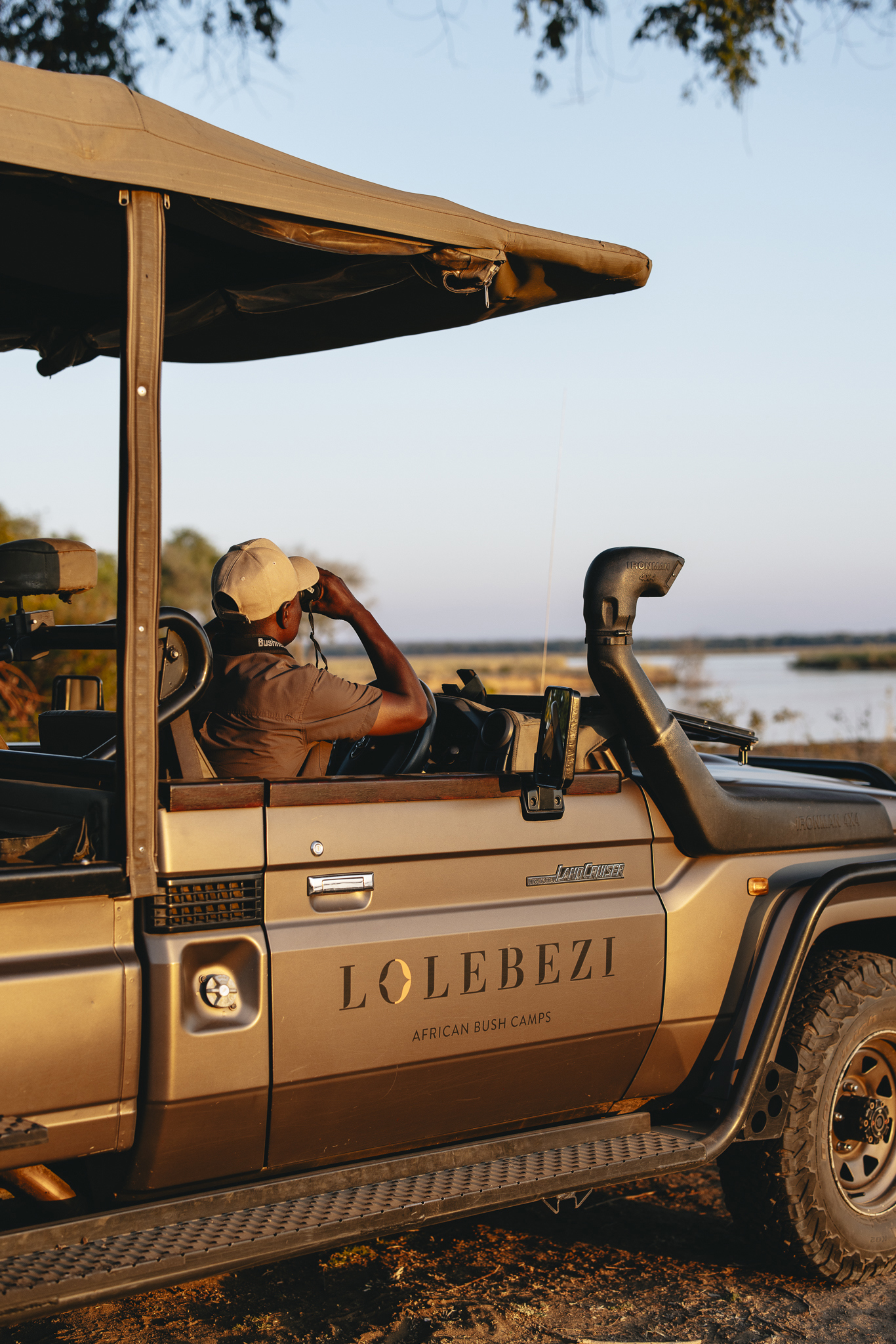 A guide at Lolebezi in a safari jeep looking out of binoculars at wildlife in the distance
