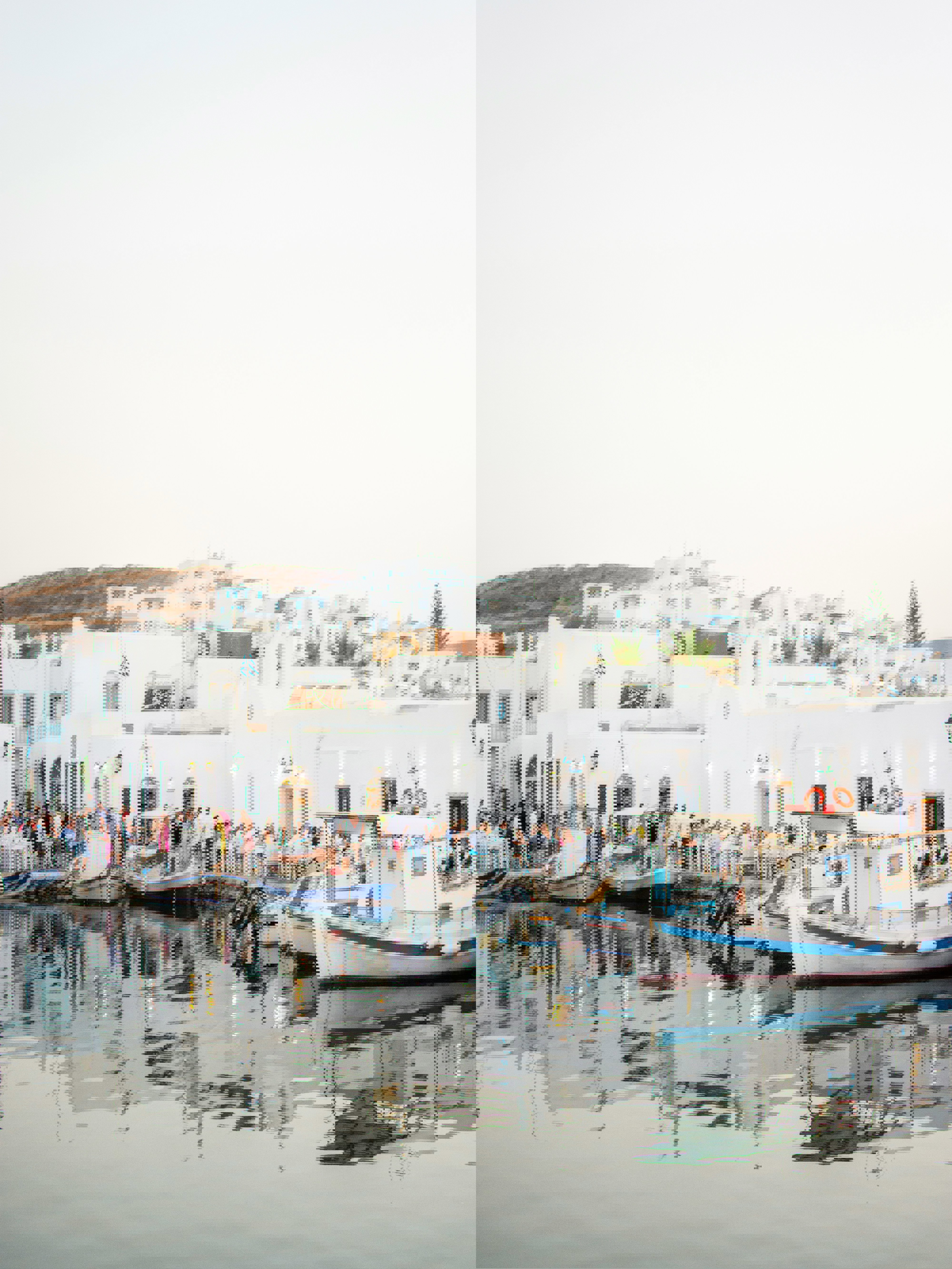 View across the Naoussa marina of people dining by the water with boats moored up at the side
