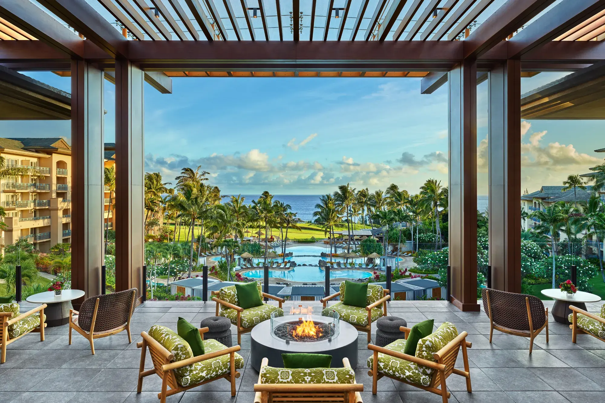 The airy terrace of the lobby at The Ritz-Carlton Maui, Kapalua featuring chairs circled around a fire pit with a view of the swimming pools and ocean beyond