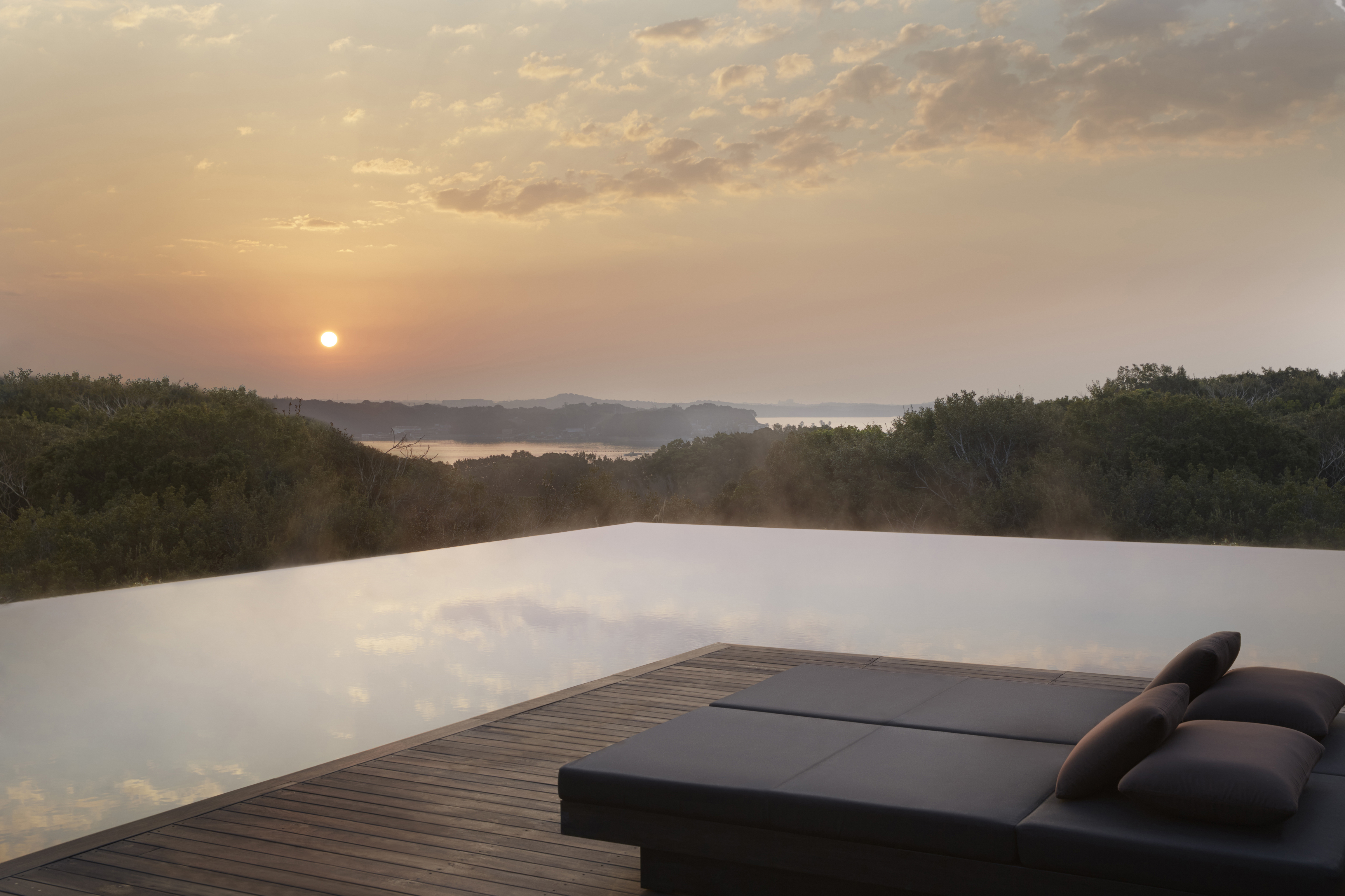 The edge of the main infinity pool at sunset with two sun loungers looking out over a sweeping view