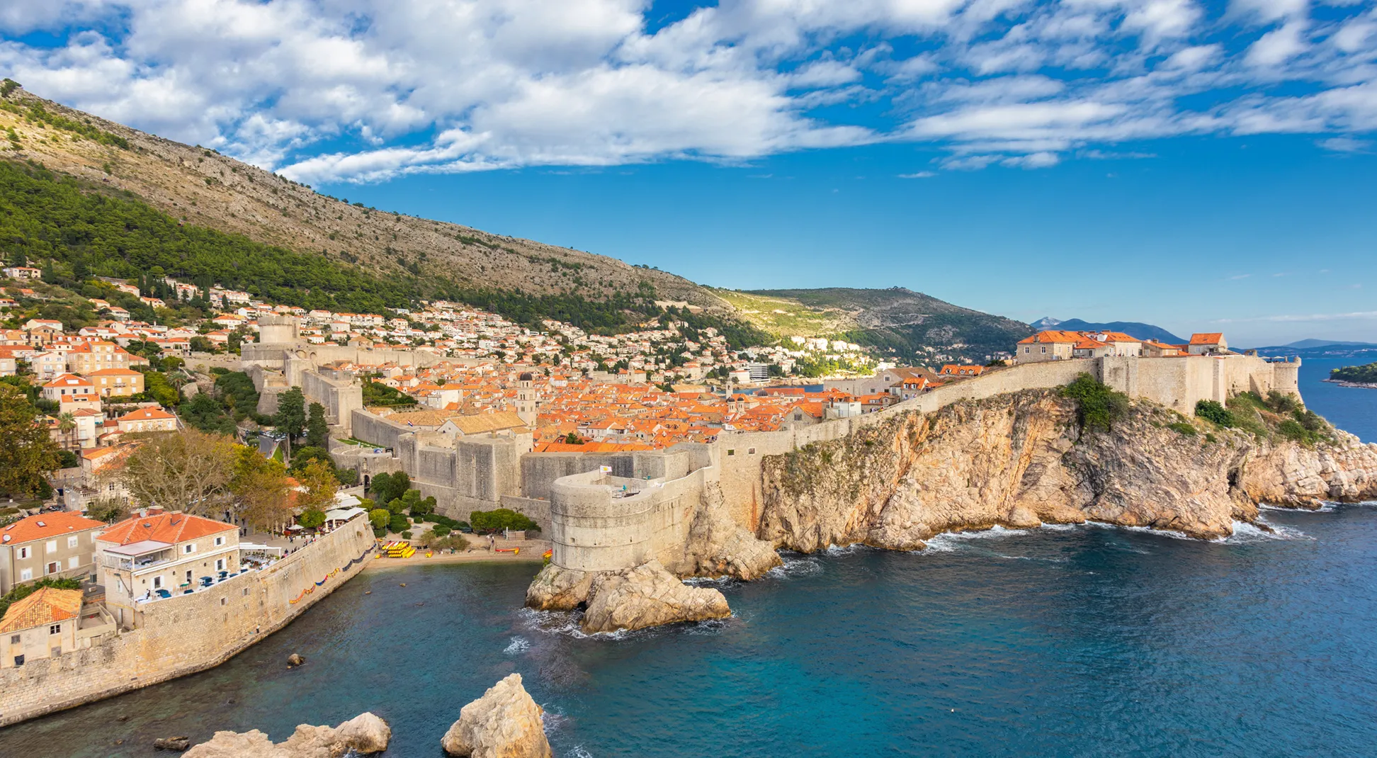 Panoramic view of Dubrovnik’s fortified old town on a rocky coastline, with stone walls, red-roofed buildings, and blue Adriatic waters.