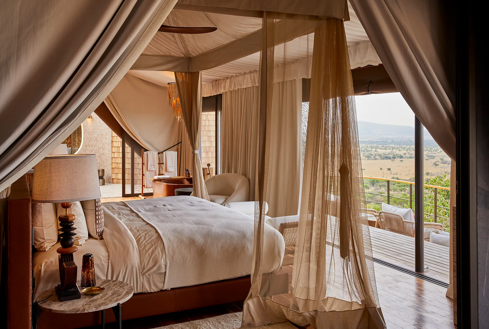 Luxurious canopy bed with sheer drapes, opening onto a private terrace with sweeping savannah views.