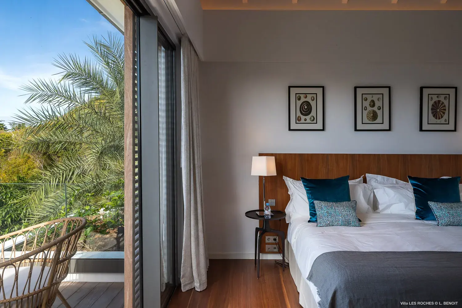 A plush bed inside a stylish bedroom at Les Roches Villa in St Barths with large sliding glass doors opening to a private terrace surrounded by tropical greenery.