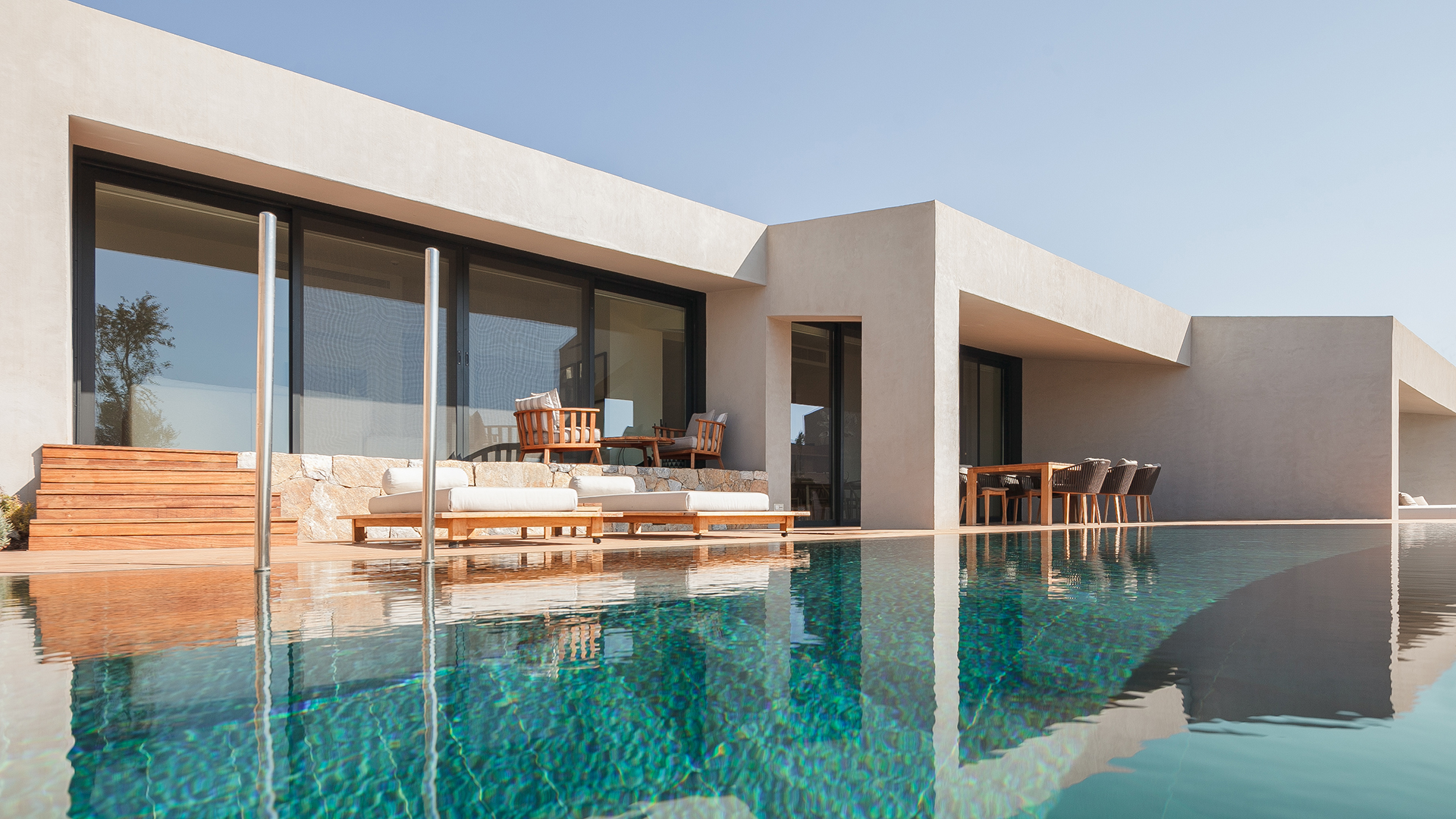 A stylish sand coloured building is flanked by an outdoor dining area and pool with loungers