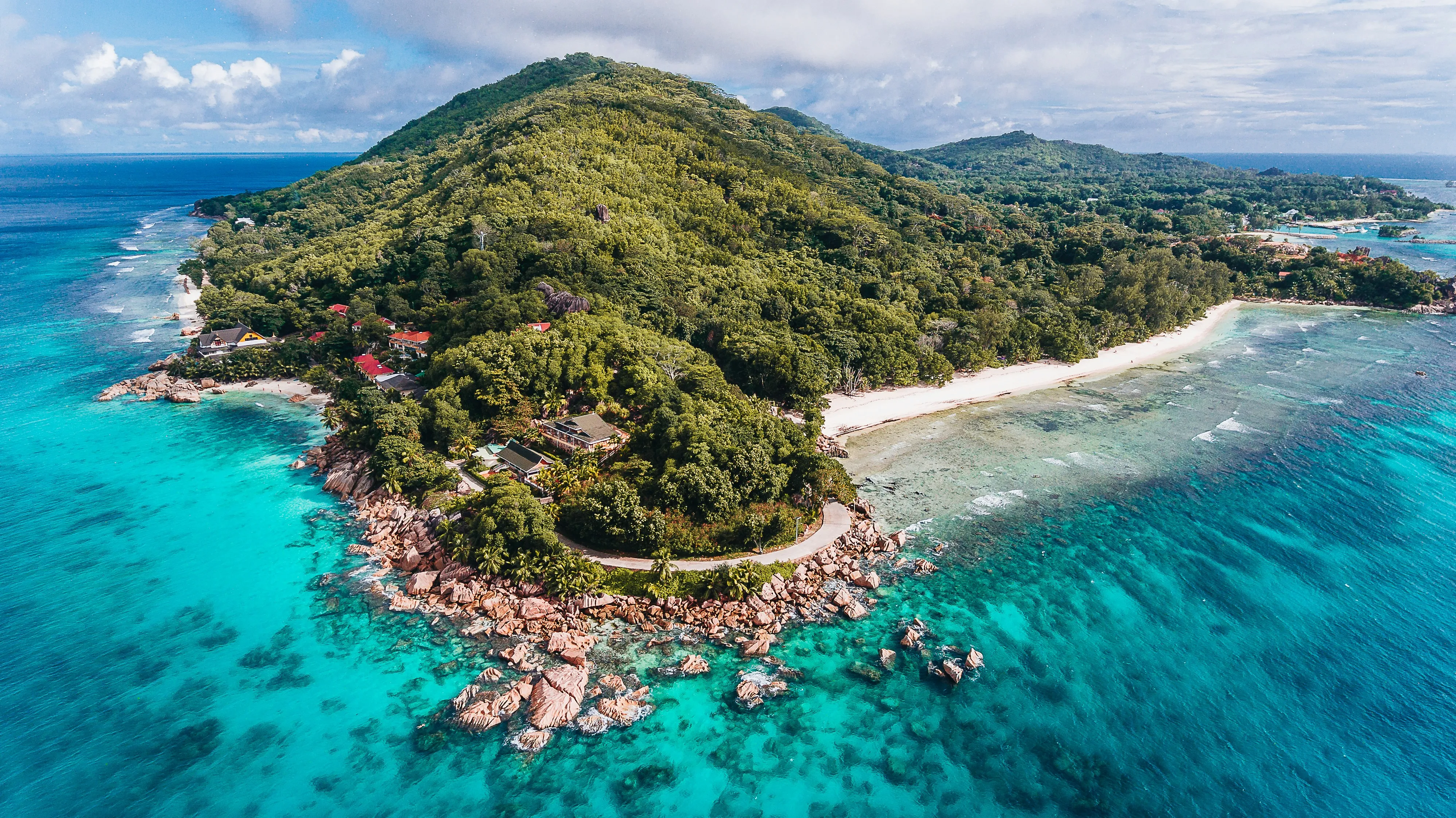 Aerial view of a La Digue Island surrounded by vibrant turquoise water, coral reefs and rocky coastline.