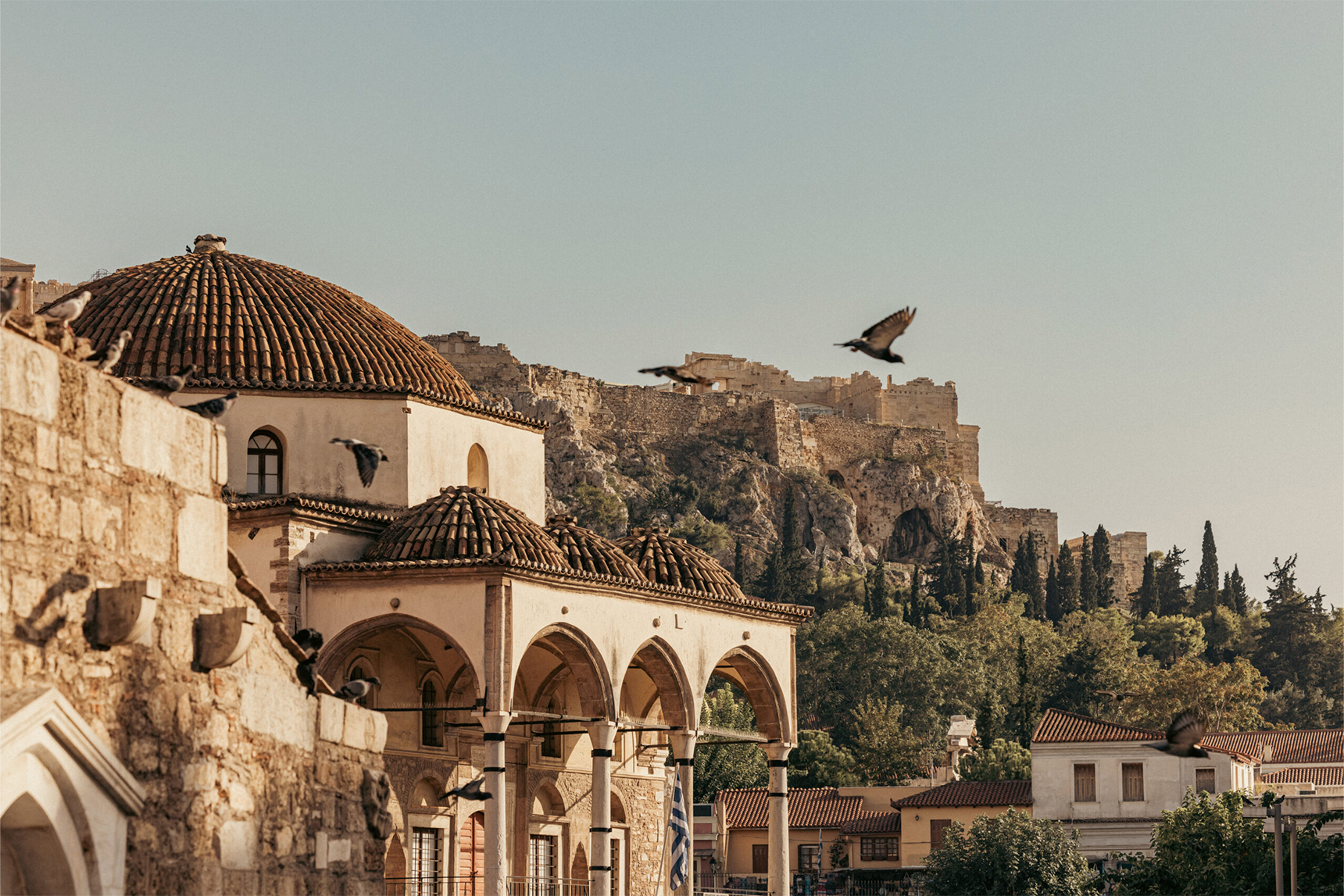Boards soar over an acient Greek street setting flanked by olive trees and domed roofs
