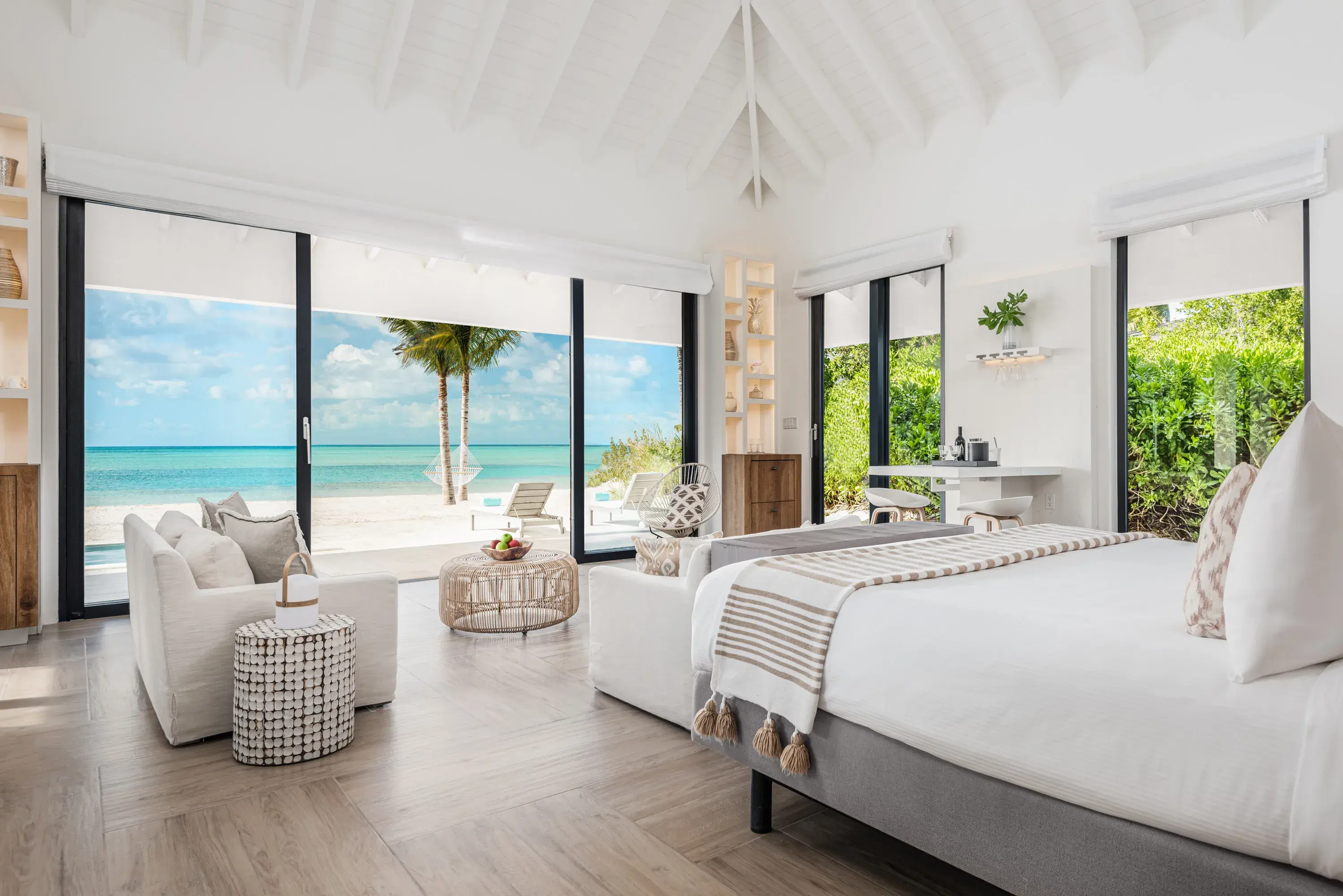 Beachfront Bungalow at Ambergris Cay in Turks & Caicos featuring comfy furniture, stylish Caribbean-style decor and large windows looking out onto the beach, ocean and greenery