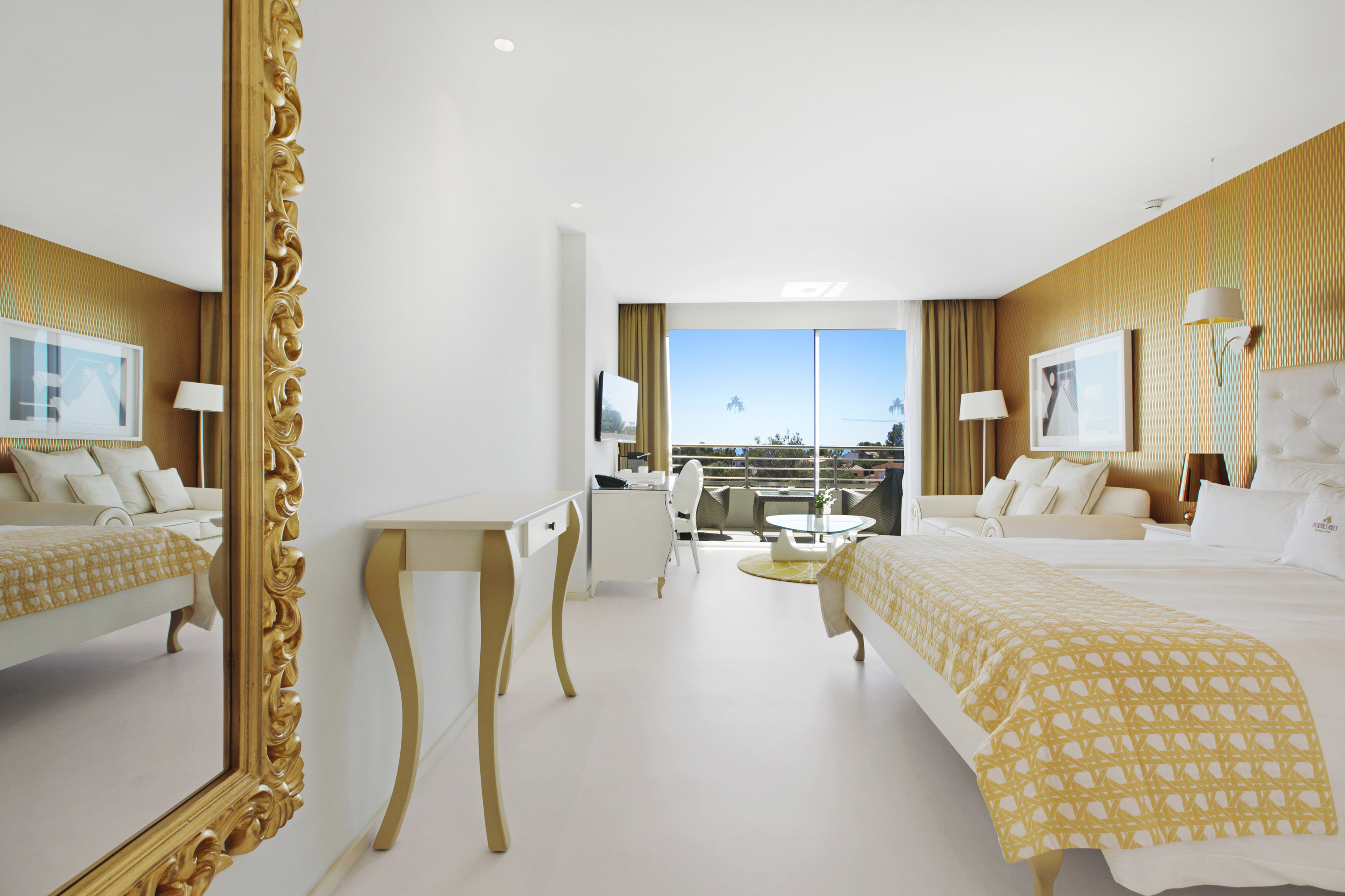 Luxurious hotel room at Portals Hills in Mallorca with ornate mirror, elegant furnishings, yellow bedding, and a balcony view of the blue sky.