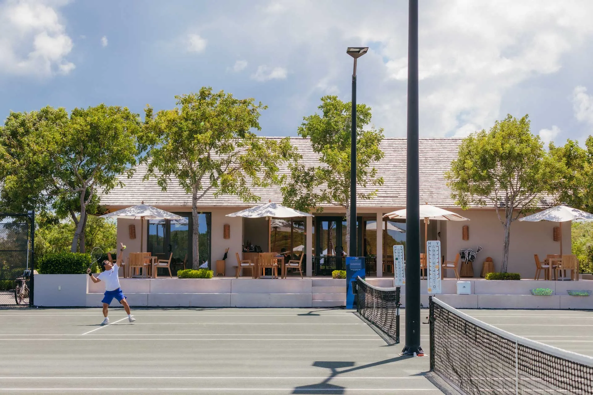 Tennis court at Amanyara with a guest playing beneath clear skies and a clubhouse terrace in the background.