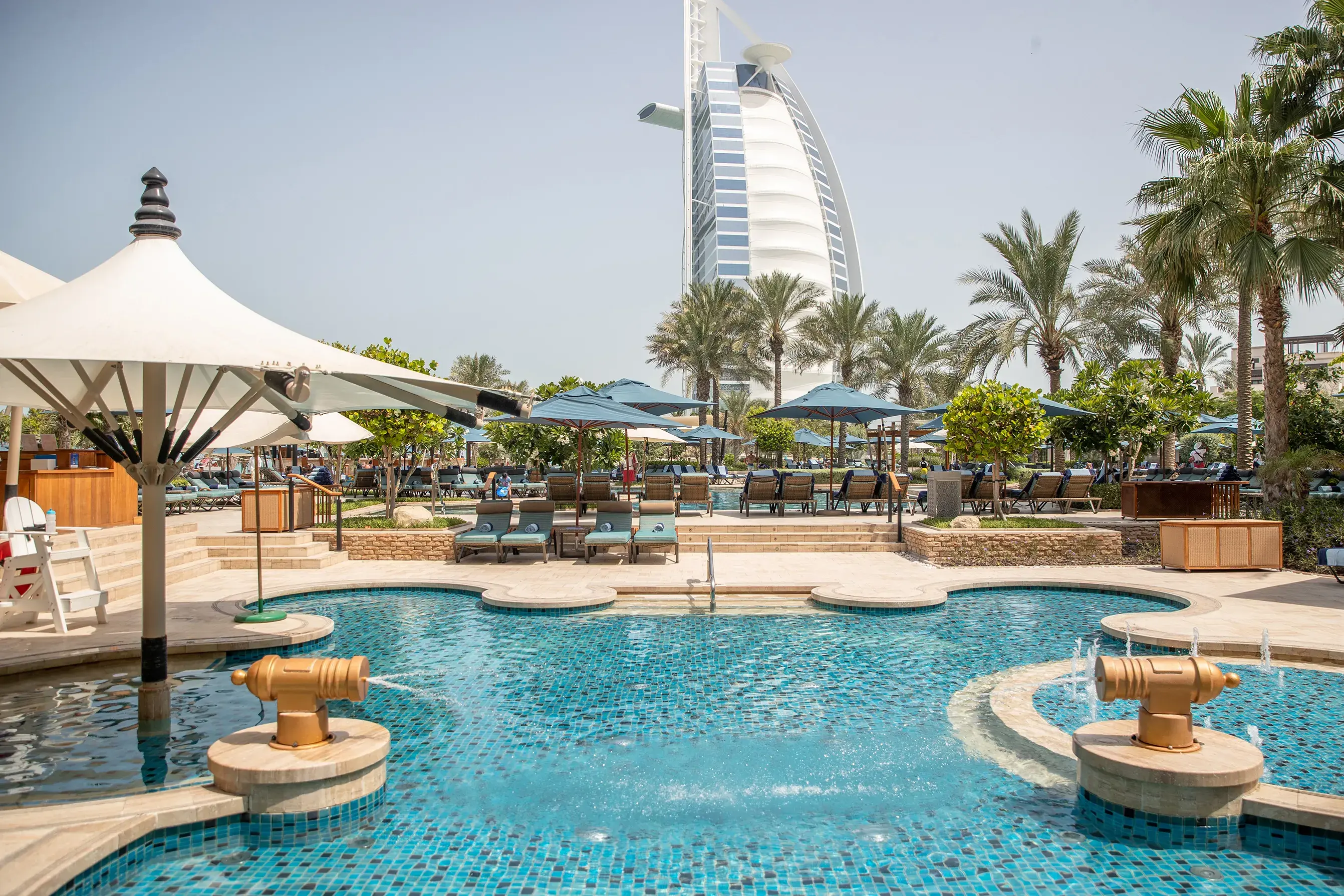 Family pool area at Jumeirah Al Naseem Dubai with shaded loungers, palm trees and views of the iconic Burj Al Arab.