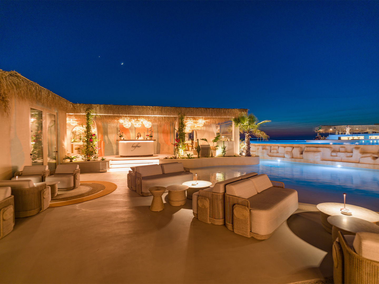 A lux bar area with cabana plush seating located next to a pool in the vening dimming light
