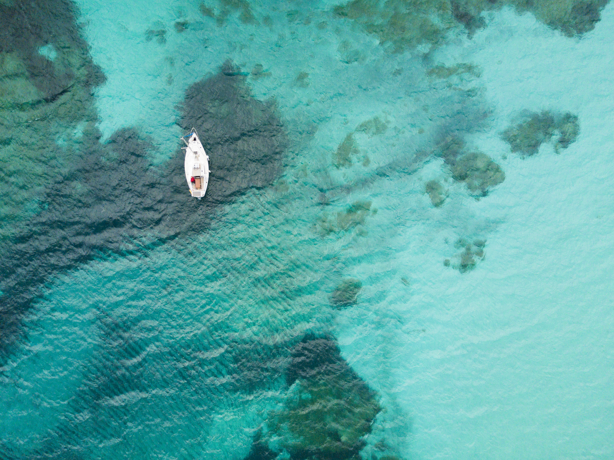 A white boat floating on clear blue water with visible underwater features.