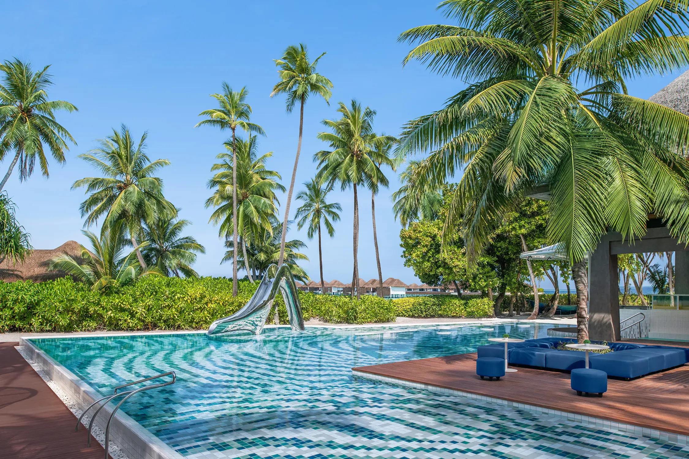 WET Deck at W Maldives featuring a stunning resort pool with signature slide sculpture, tropical palm-lined surroundings, luxury lounge seating, and views across the island paradise