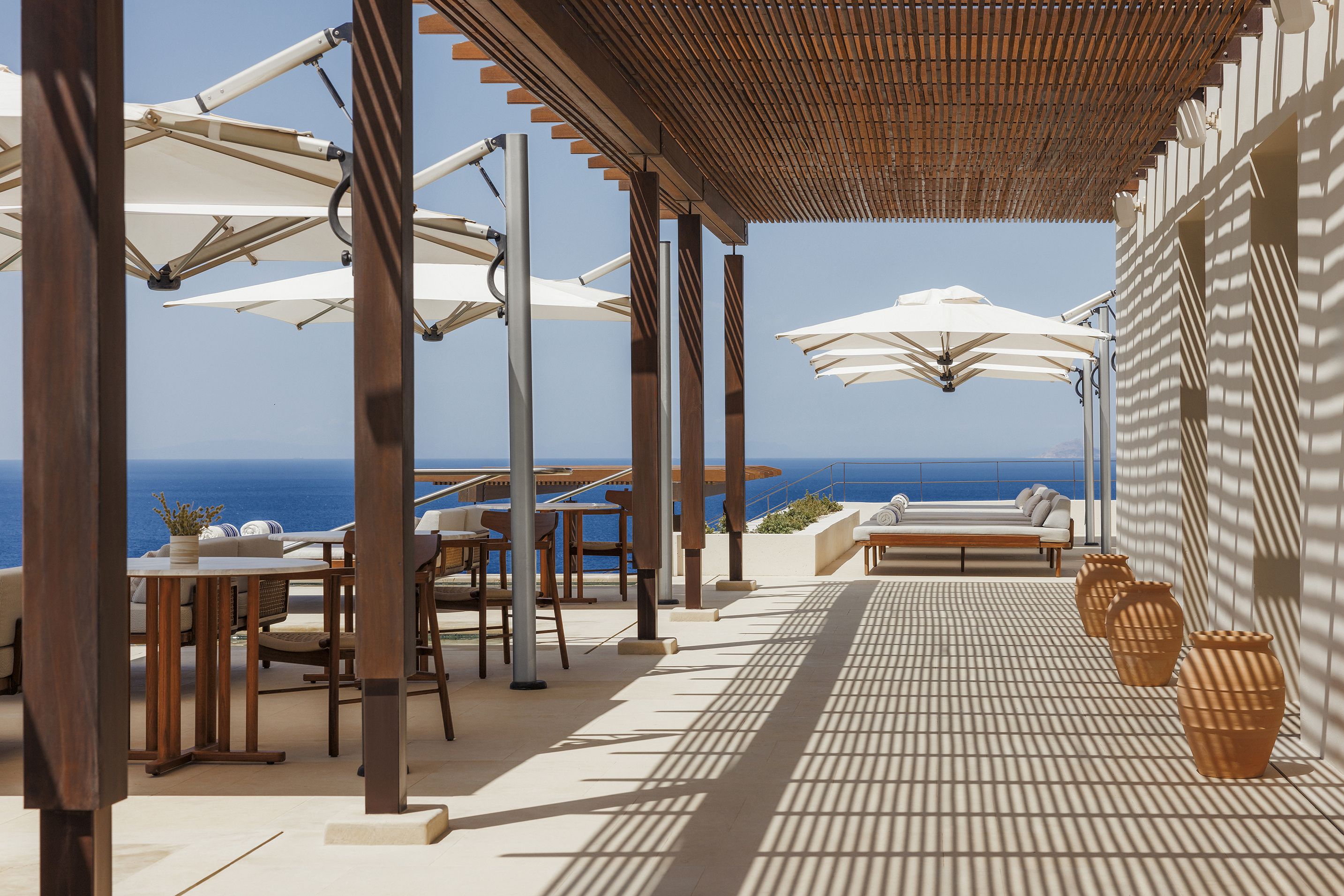 Walkway covered by wooden canopy by hotel pool with white umbrellas over seating areas
