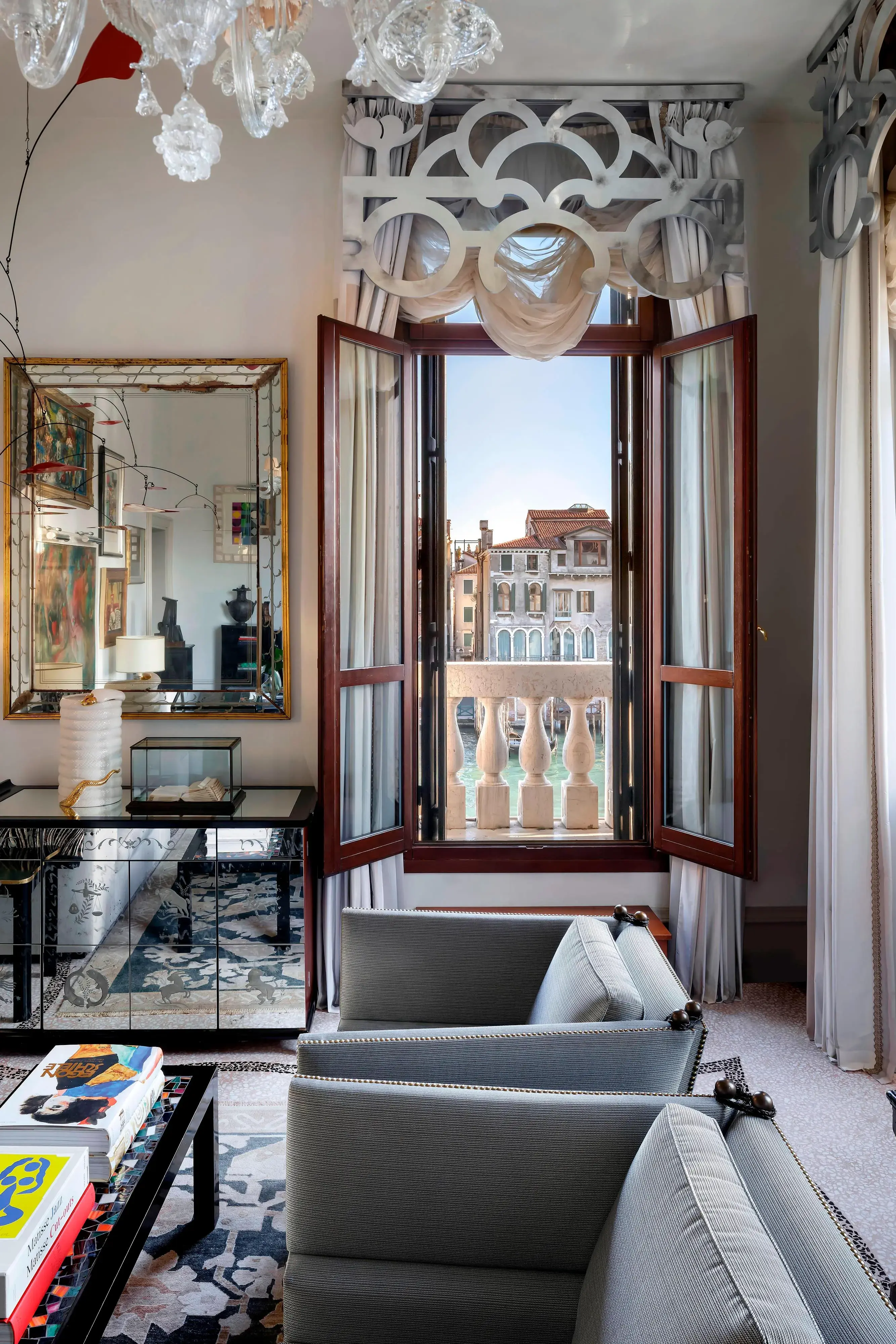 Elegant sitting area at The Gritti Palace in Venice with plush armchairs, decorative mirror, and open window overlooking the Grand Canal.