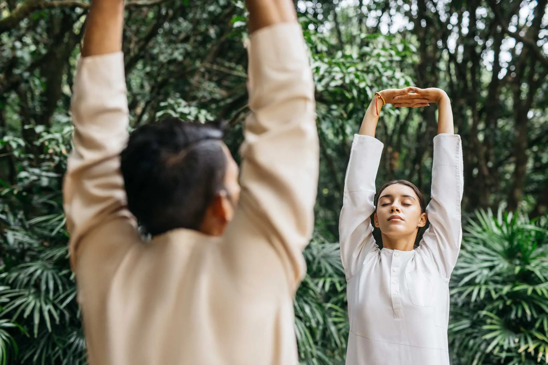 A man and woman facing each other stretching their arms to the sky