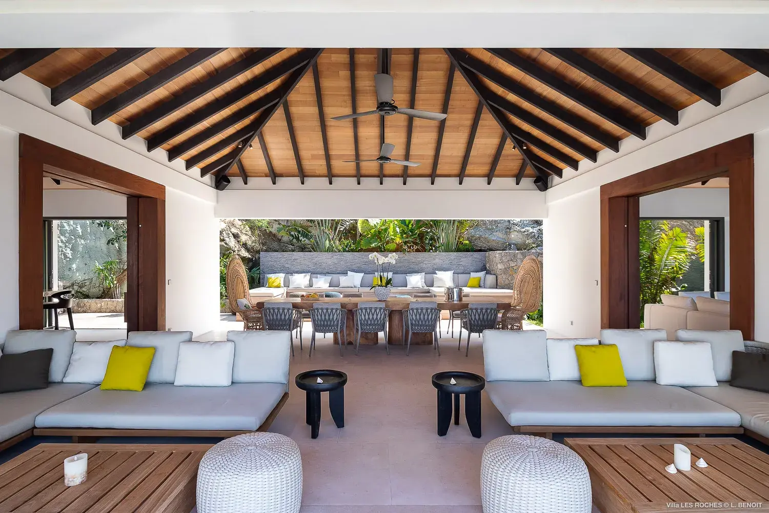 Open‑air living and dining pavilion at Les Roches Villa in St Barths featuring vaulted wooden ceilings, modern lounge seating and tropical garden views.
