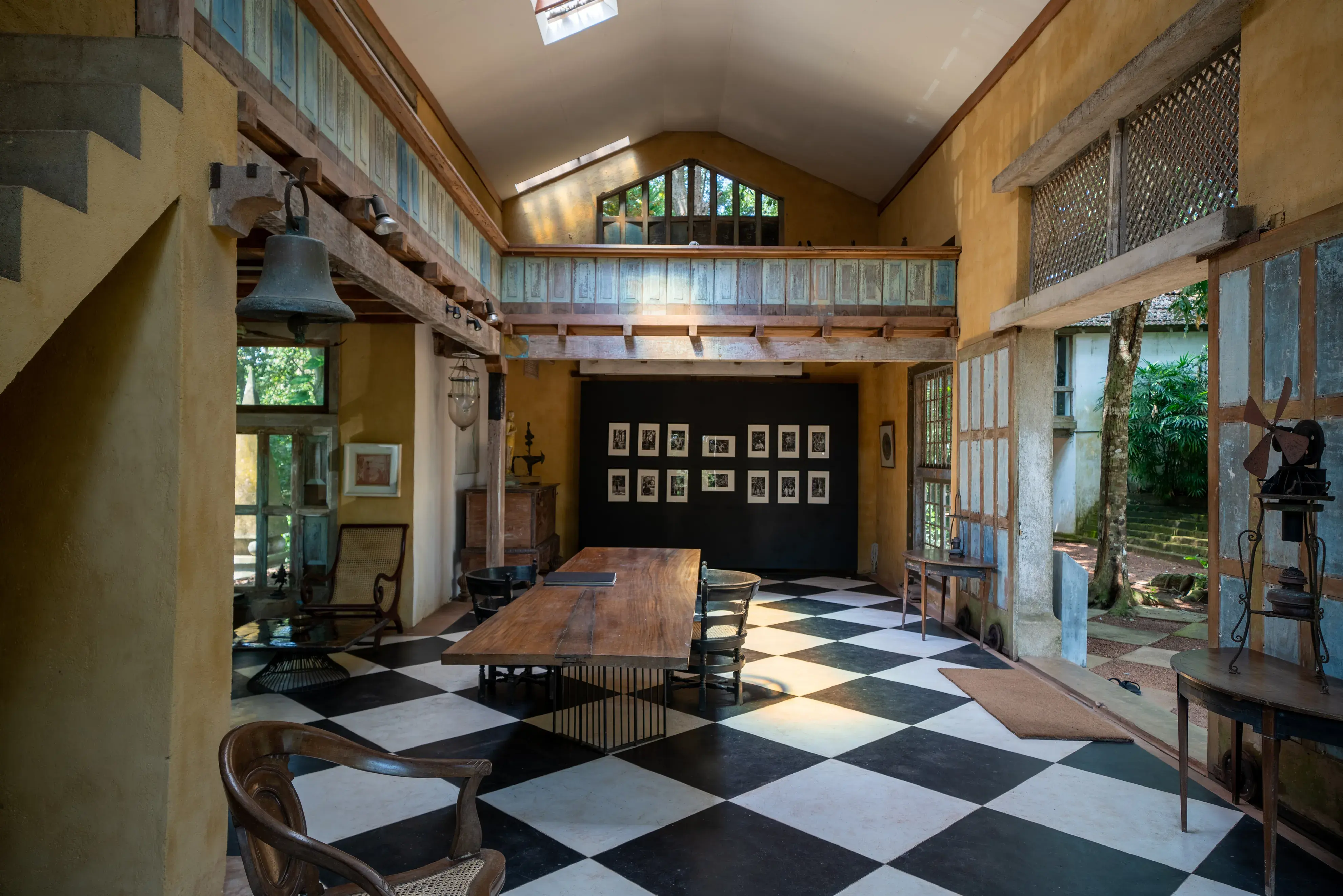Rustic interior of Lunuganga estate in Sri Lanka featuring high ceilings, checkered flooring, wooden furniture, and garden views through large windows.