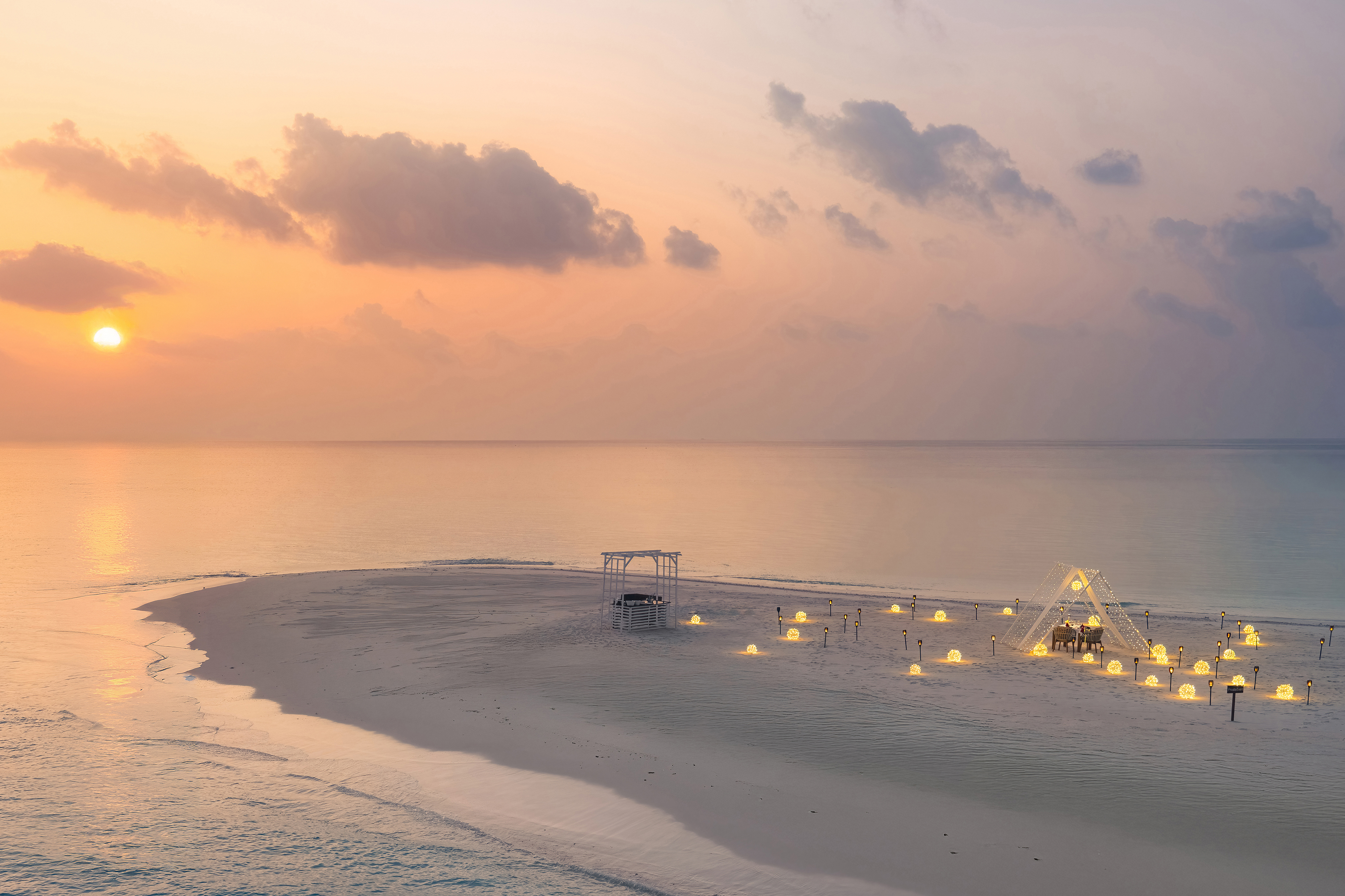 Sunset view of a serene beach at InterContinental Maldives with illuminated cabanas set up for dinner and a tranquil ocean backdrop.