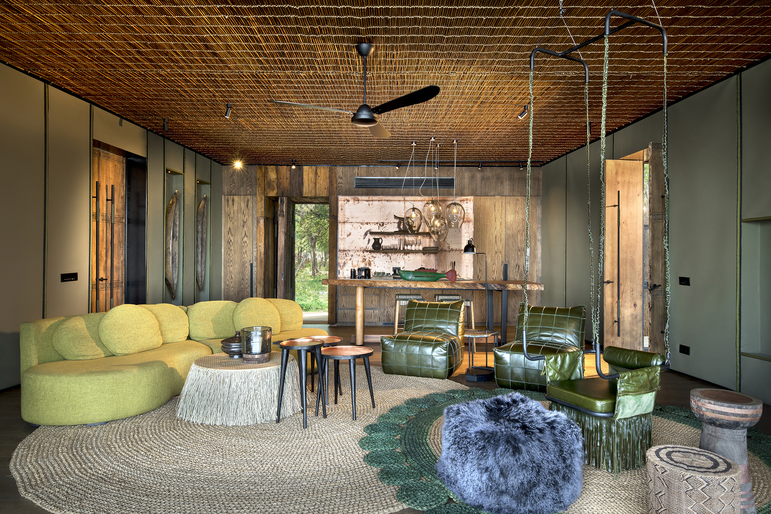 The cosy lounge of a suite at Lolebezi featuring comfy furniture in green shades, woven soft decor and artifacts on the back wall