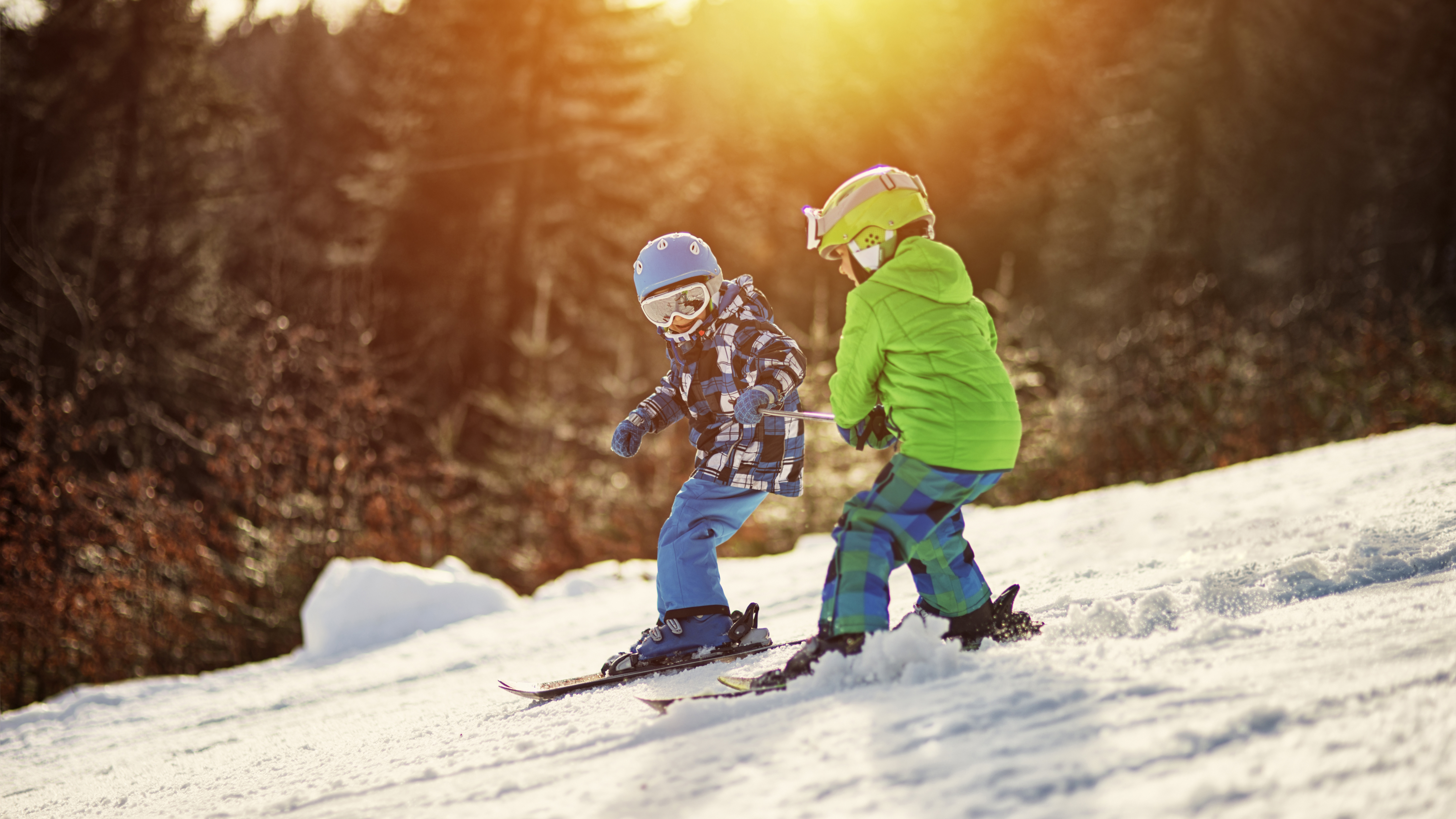 Two children wearing blue and green skiing during sunset 