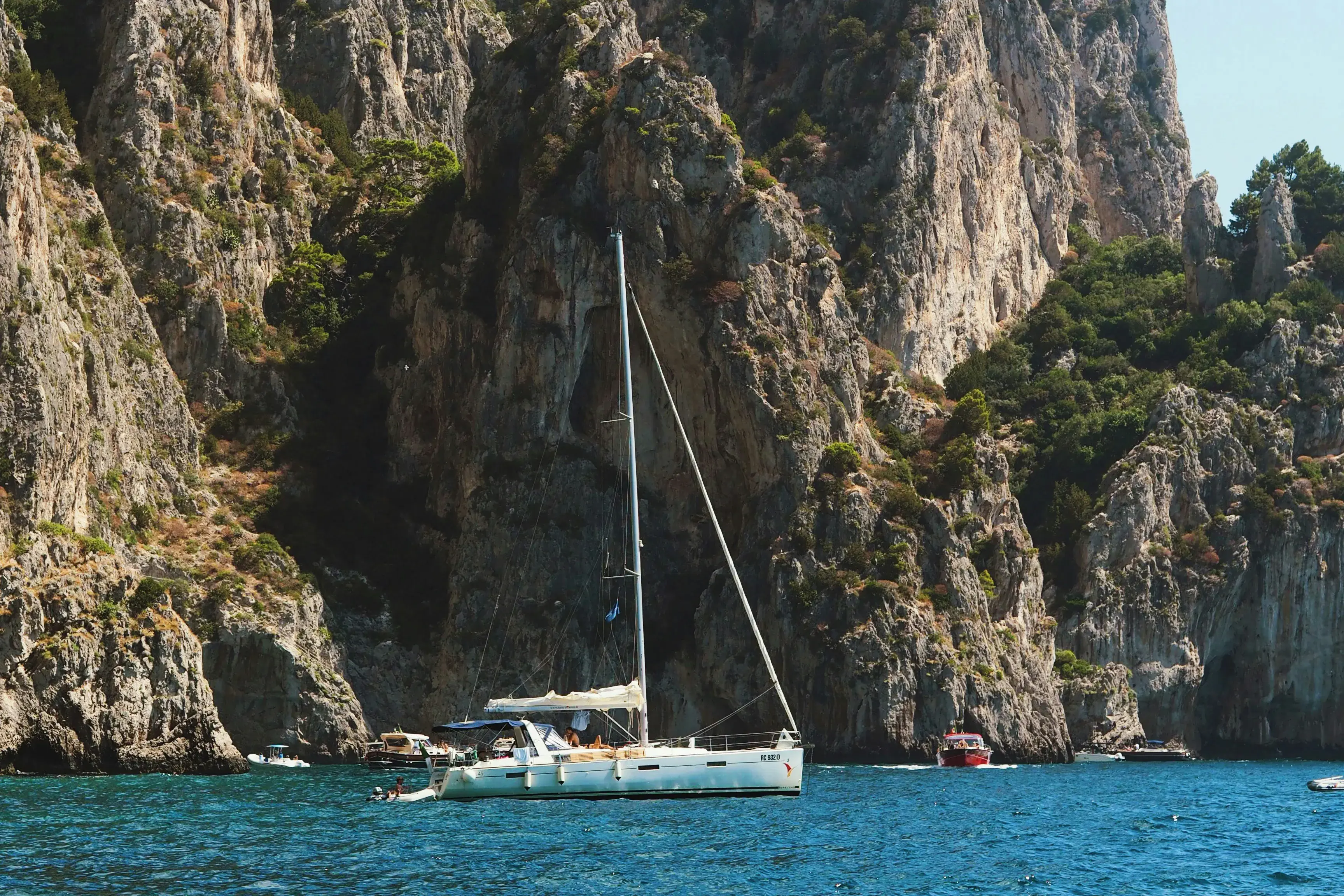 White sailboat anchored near towering limestone cliffs and turquoise waters off the coast of Capri, Italy.