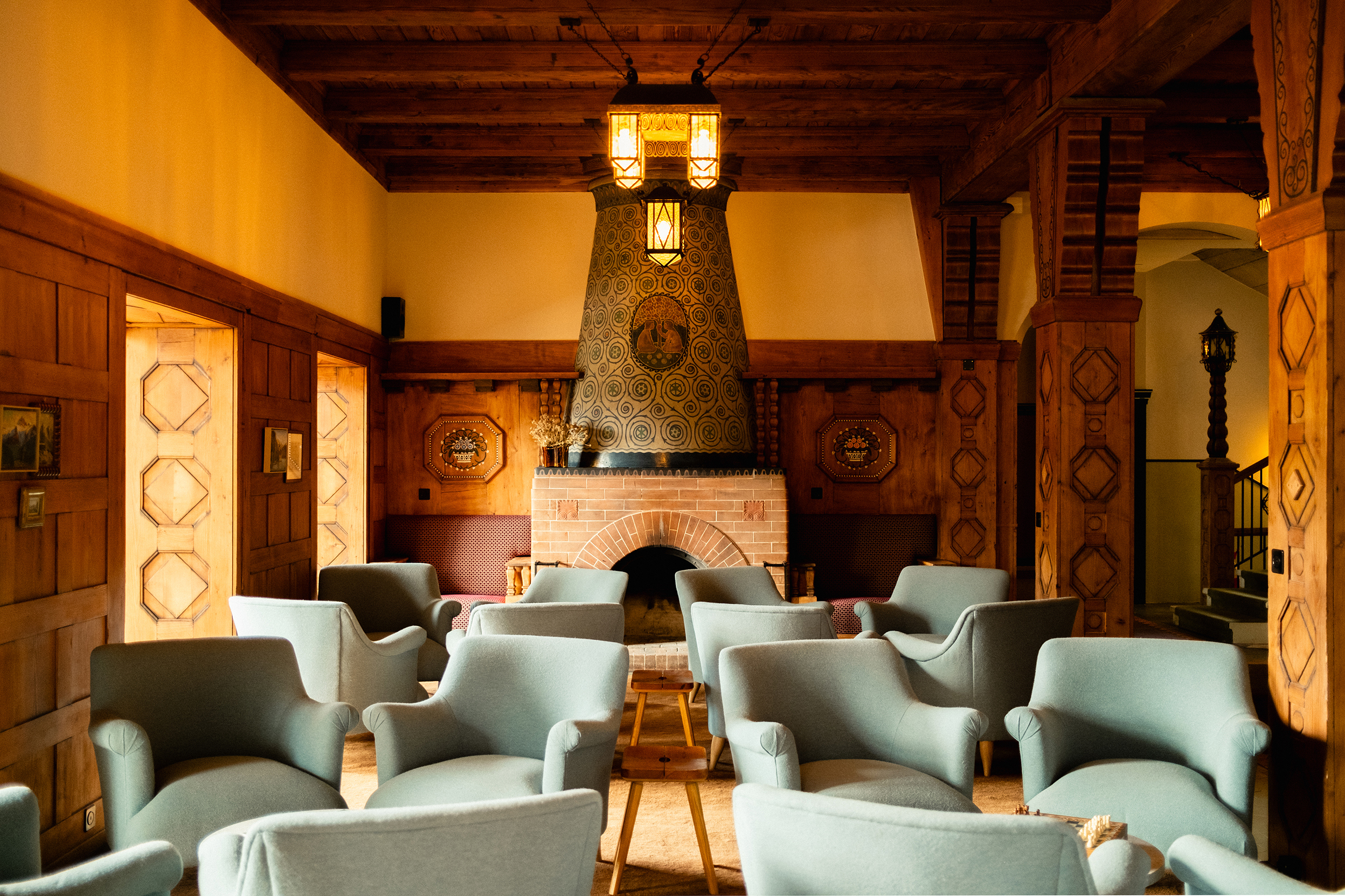 The lounge area of a lobby with comfy blue chairs set out in front of a large fireplace surrounded by decorative wood panelling