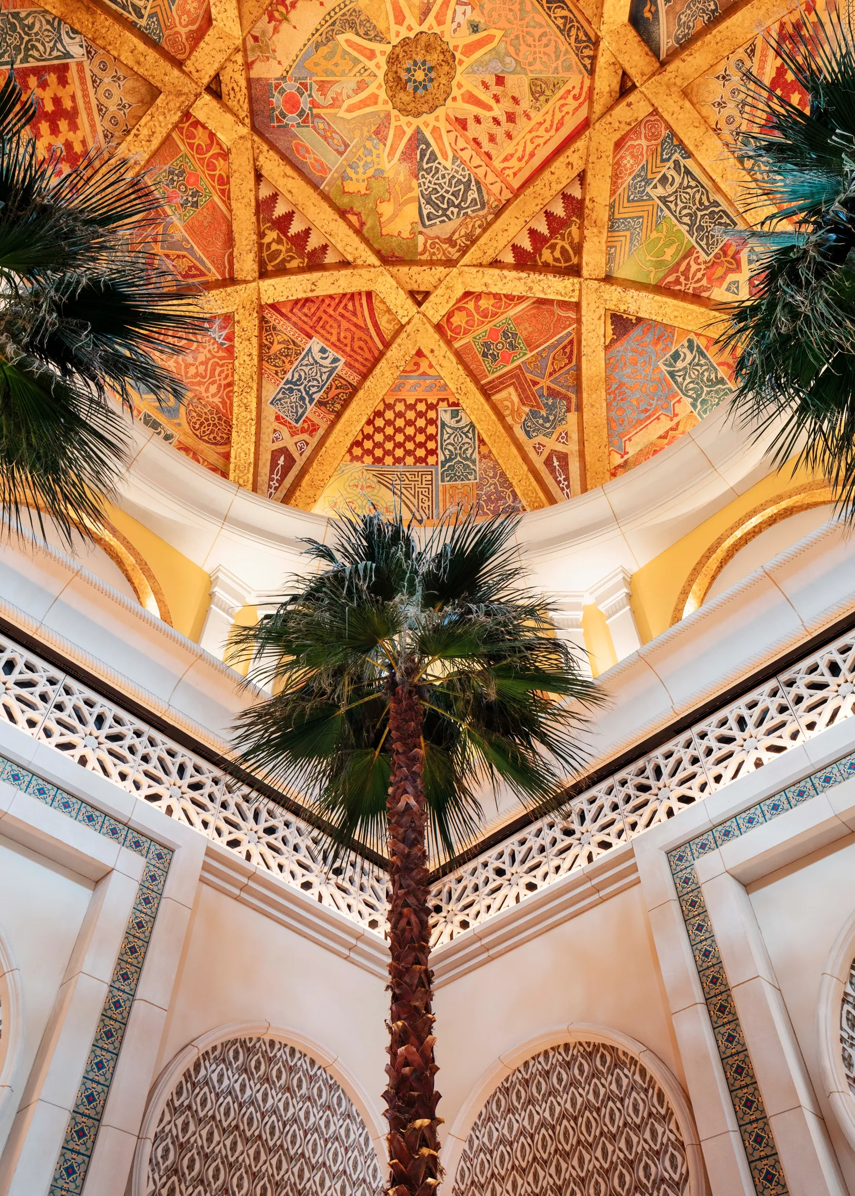 Palm tree in an ornate courtyard with patterned walls and a colorful domed ceiling