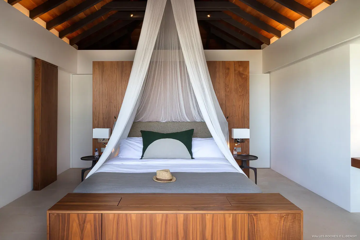 Stylish master bedroom at Les Roches Villa in St Barths featuring a wooden canopy bed with draped netting and vaulted ceiling design.