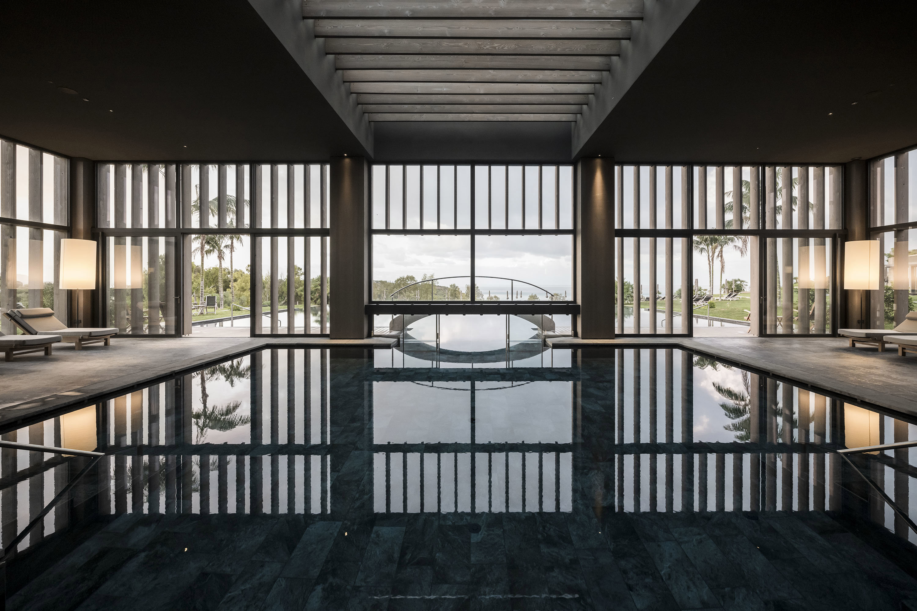 Vast indoor pool flanked by loungers with greenery through the windows