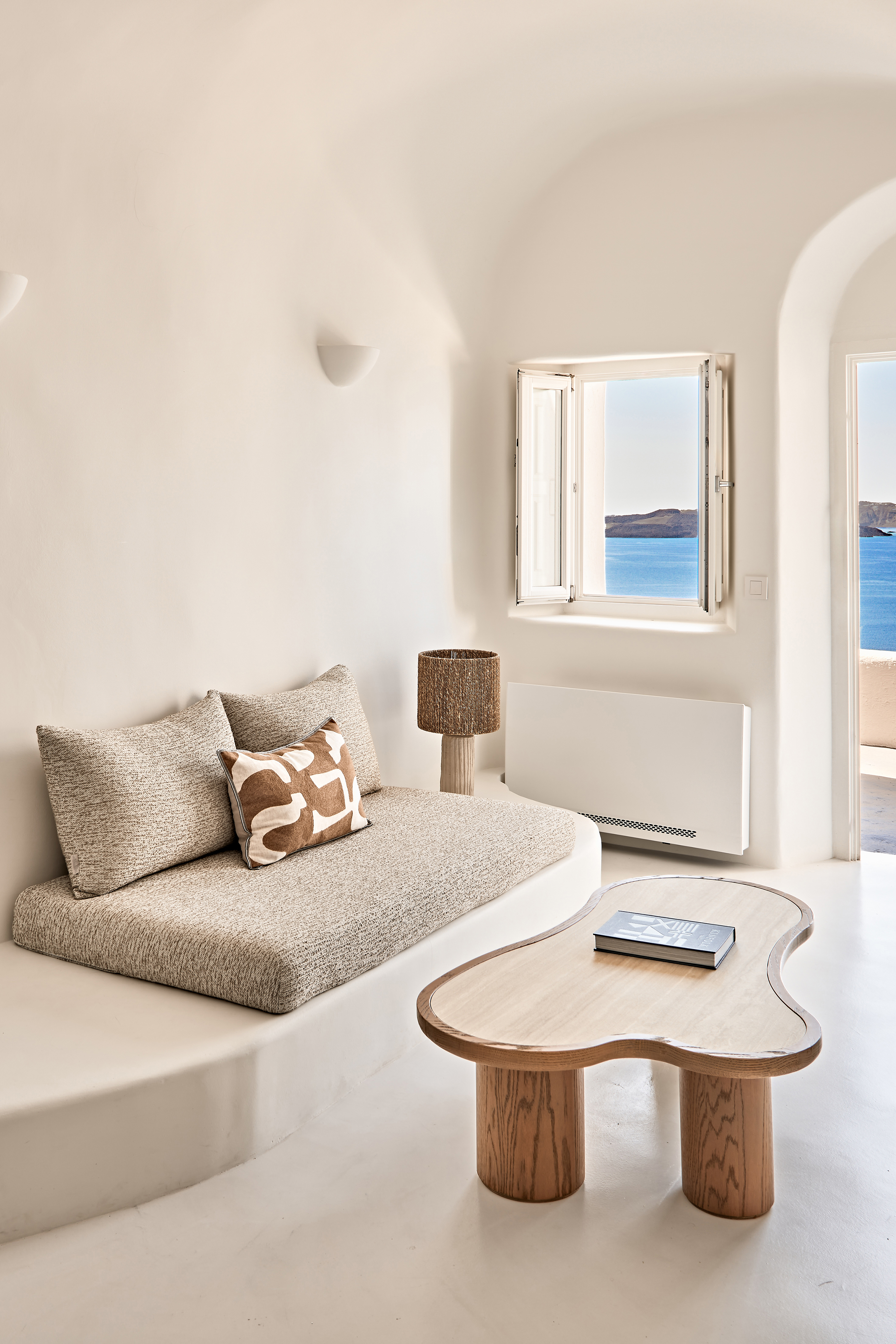 A stylish all-white suite featuring a sofa and wooden coffee table with a window looking out to the landscape