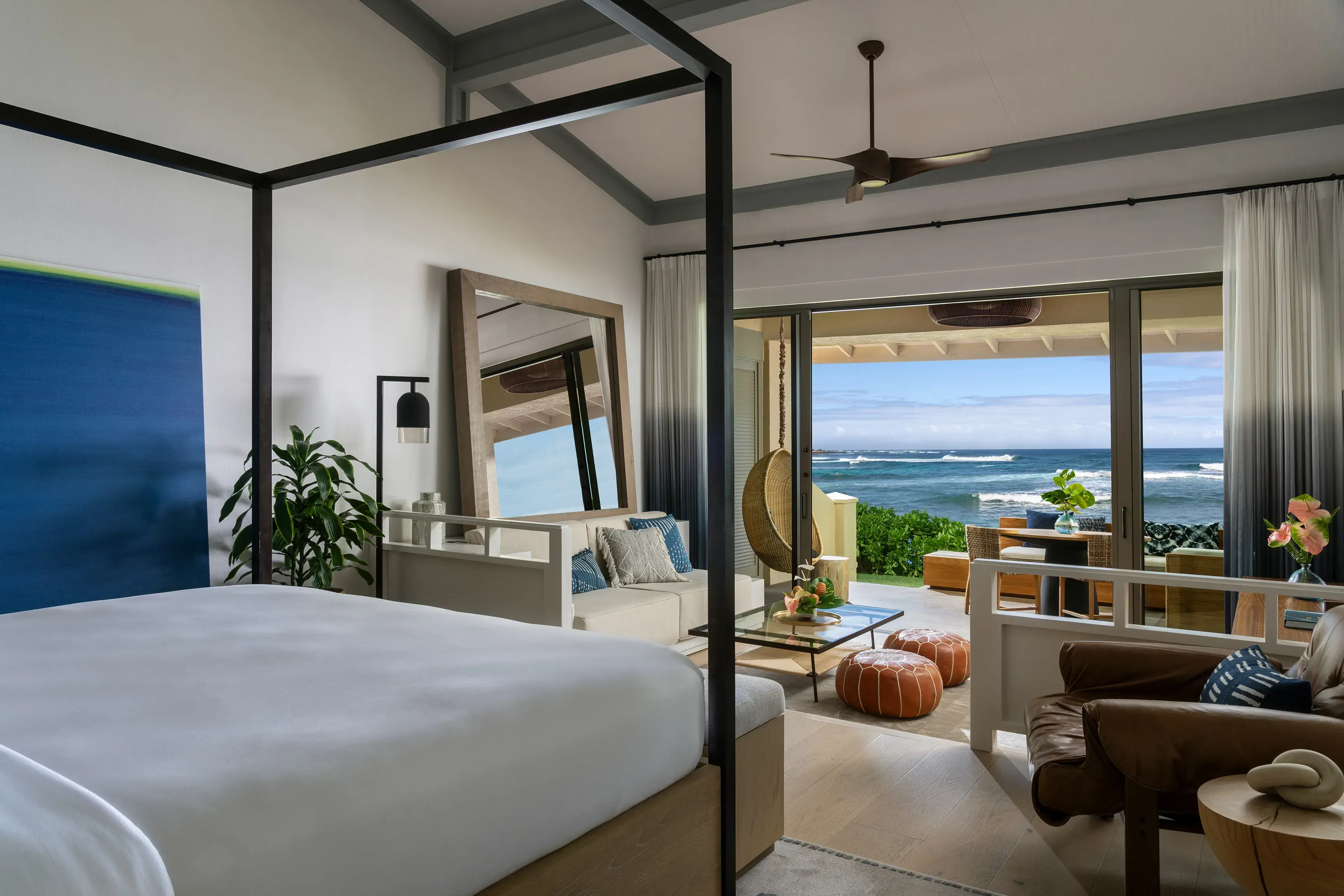 An Oceanfront Bungalow at Ritz-Carlton Turtle Bay featuring a king size four poster bed facing a relaxed lounge area and large windows looking out to sea