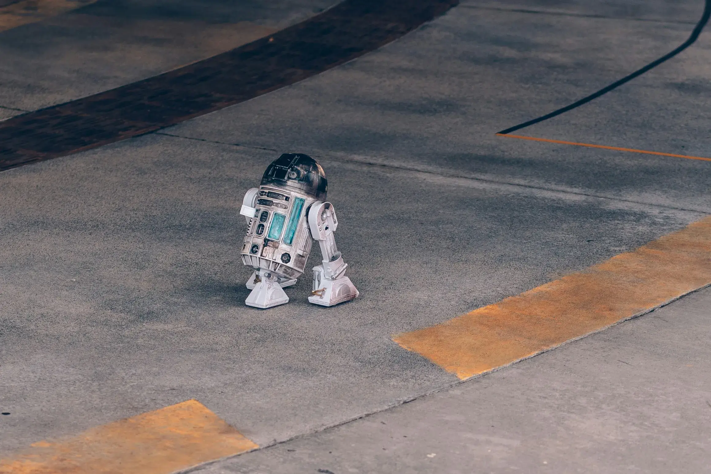 Small astromech-style robot toy positioned on a concrete surface with painted yellow markings.