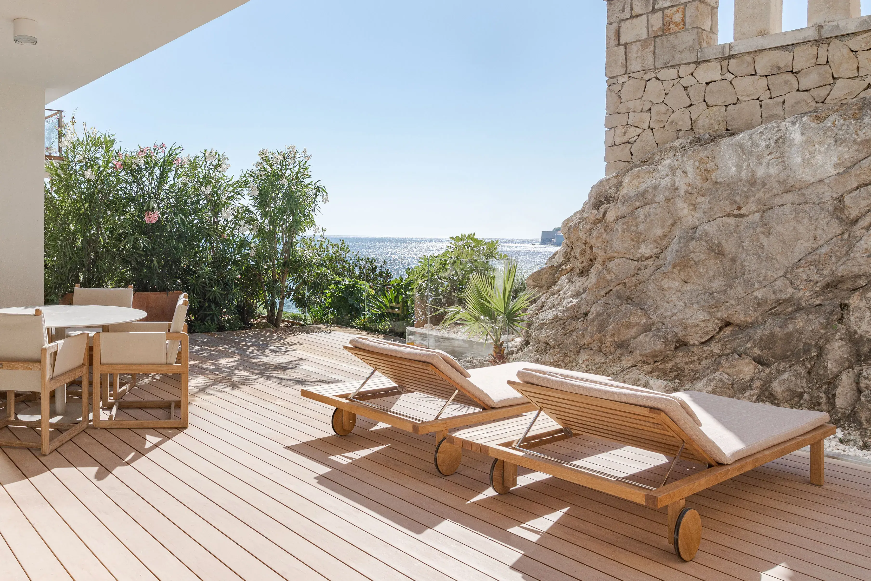 Terrace of Amor Suite at Villa Dubrovnik in Croatia featuring sun loungers and dining set on a wooden terrace overlooking stone ruins and a sea view