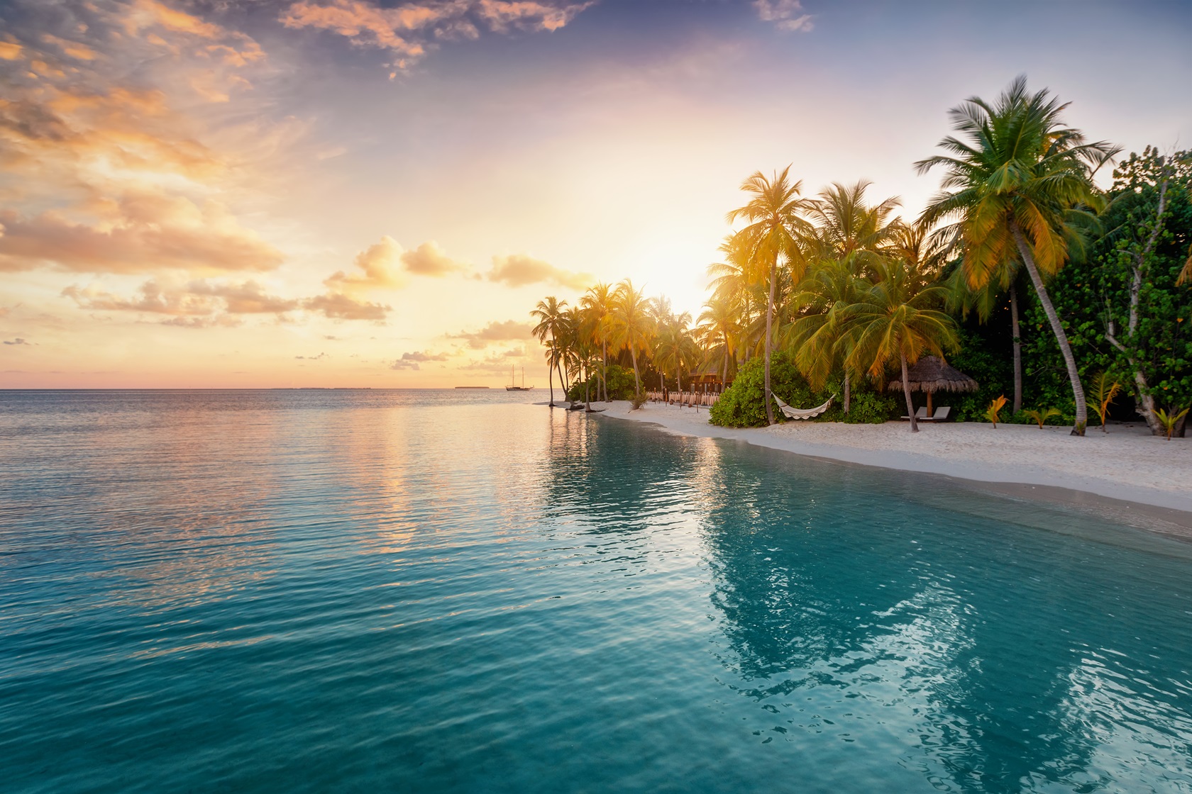 A tropical Maldivian beach at sunset with palm trees along the shore and calm ocean waters reflecting the colorful sky.