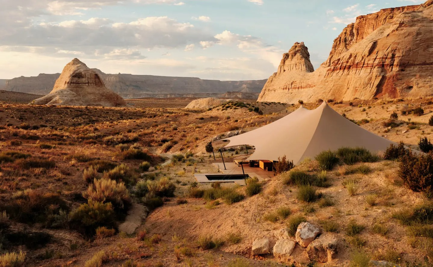 Luxury canvas tent set in a desert landscape with sandstone formations and dry scrub under soft evening light.