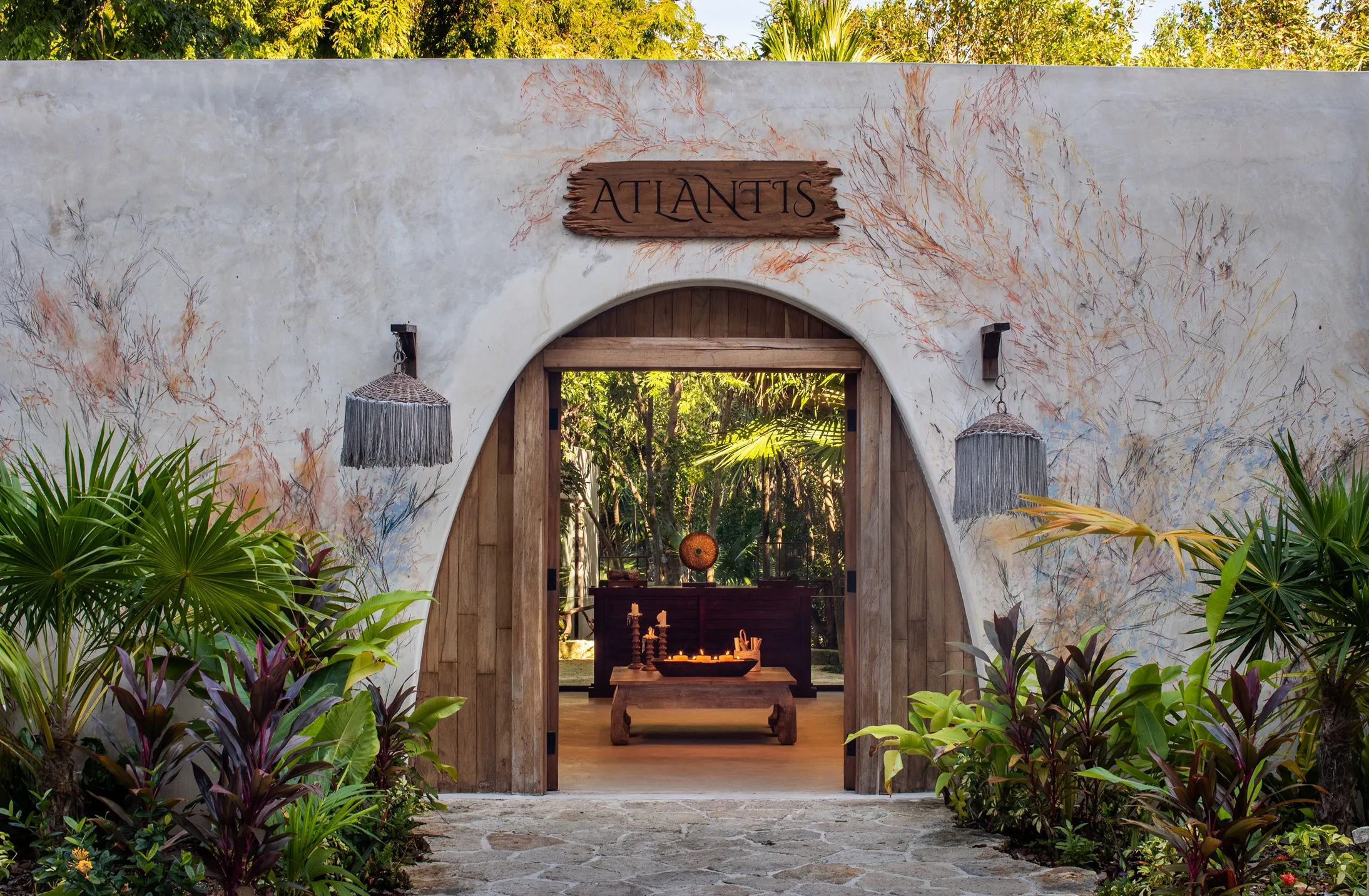 Arched spa entrance framed by tropical plants with “Atlantis” sign above wooden doors.