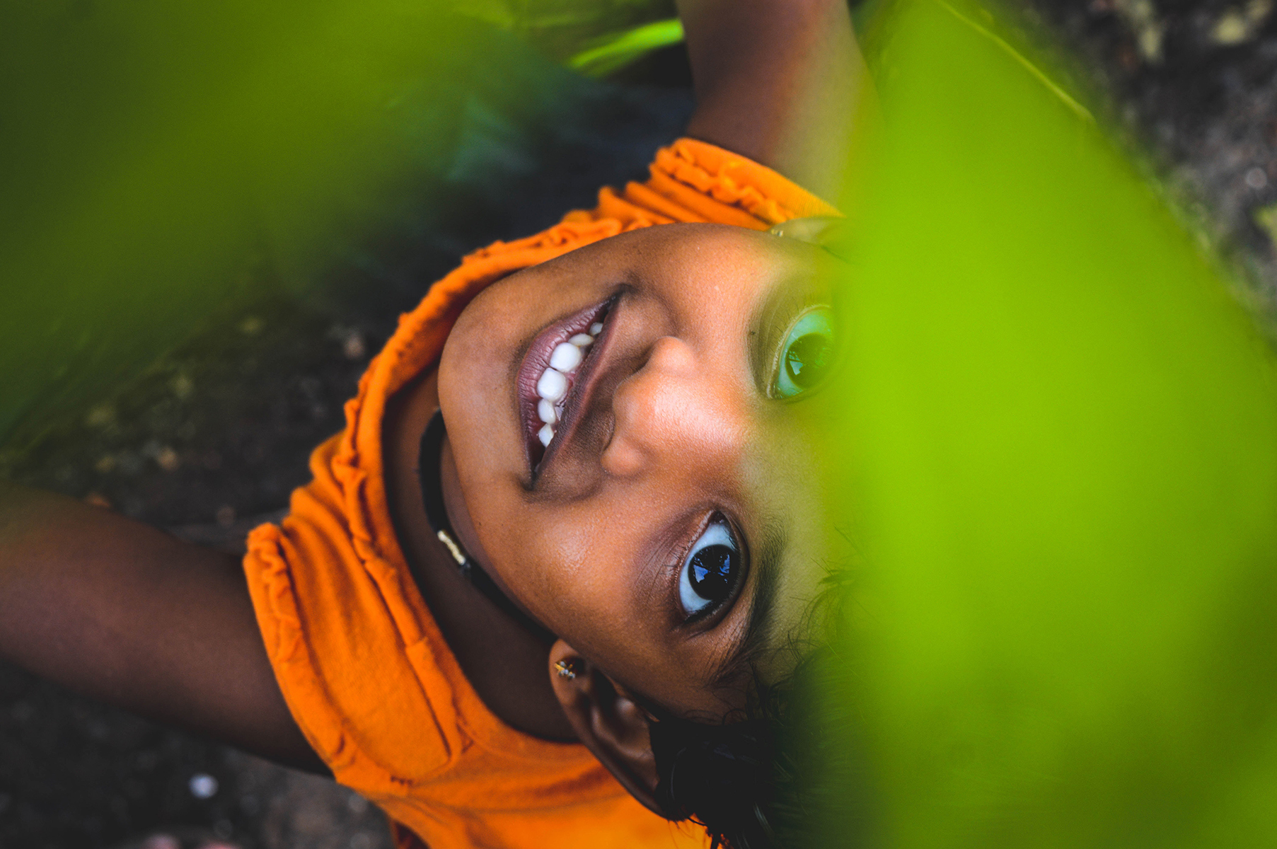 Girl looking up through green leaves and smiling