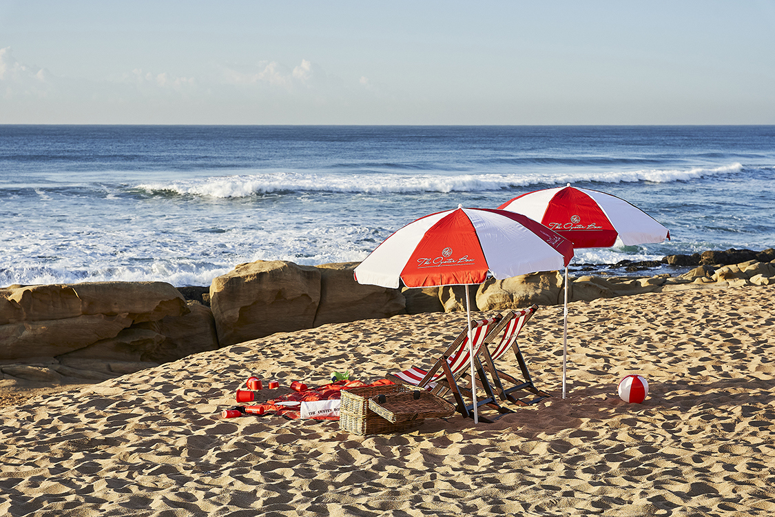 Red and white beach furniture set up on the sand with rocks in front and the ocean in the background