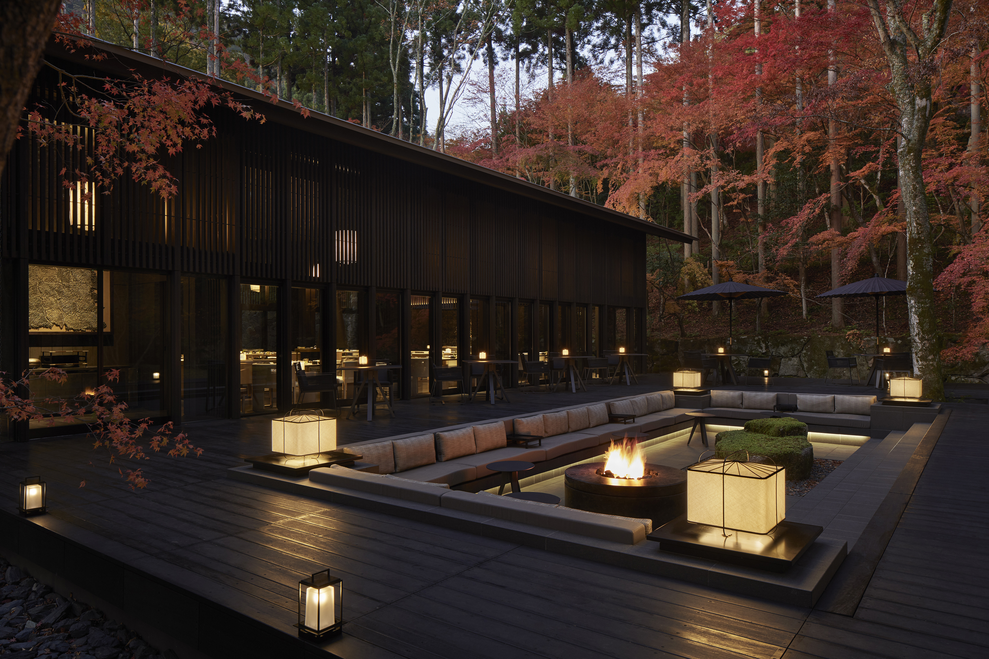The exterior of the Living Pavilion at Aman Kyoto featuring a fire pit and seating area surrounded by lanterns beneath red autumn trees