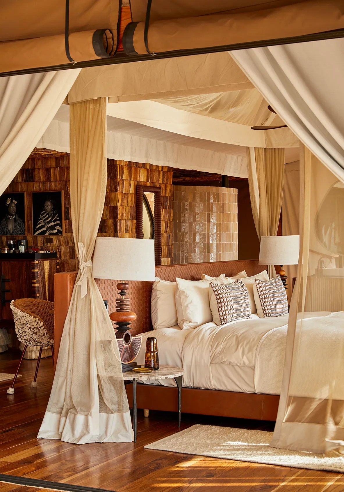 Canopy bed with sheer drapes in a luxurious safari-style suite featuring warm wood finishes and woven furnishings.