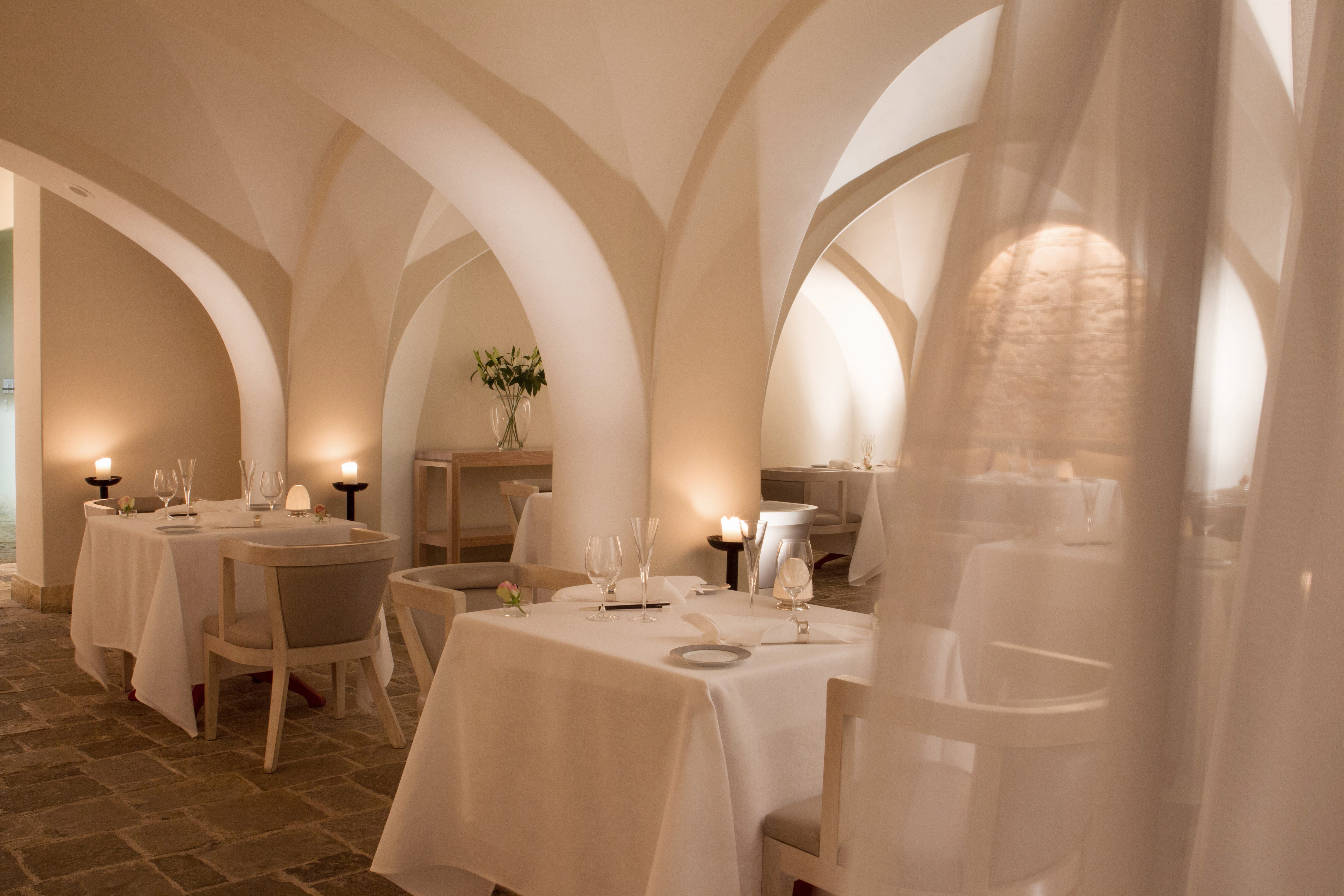 Basiliko Restaurant at Anassa in Cyprus featuring modern tables set for dinner beneath white arched ceilings with a linen curtain blowing in the corner