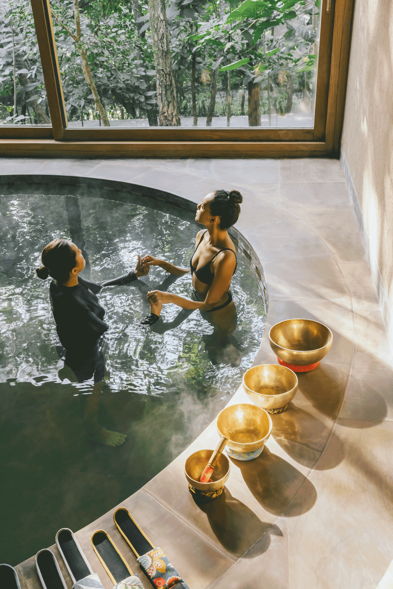 Two guests standing in a warm indoor pool at Six Senses Vana, with singing bowls placed beside the water.