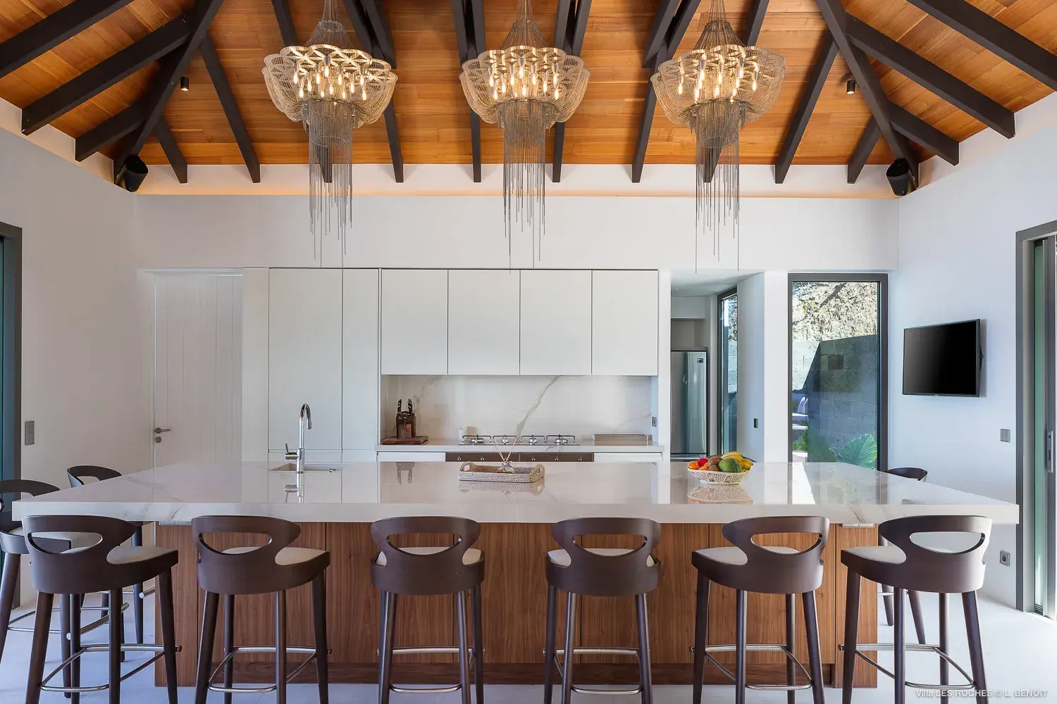 Modern designer kitchen at Les Roches Villa in St Barths featuring vaulted wooden ceilings, a large marble island and contemporary seating.