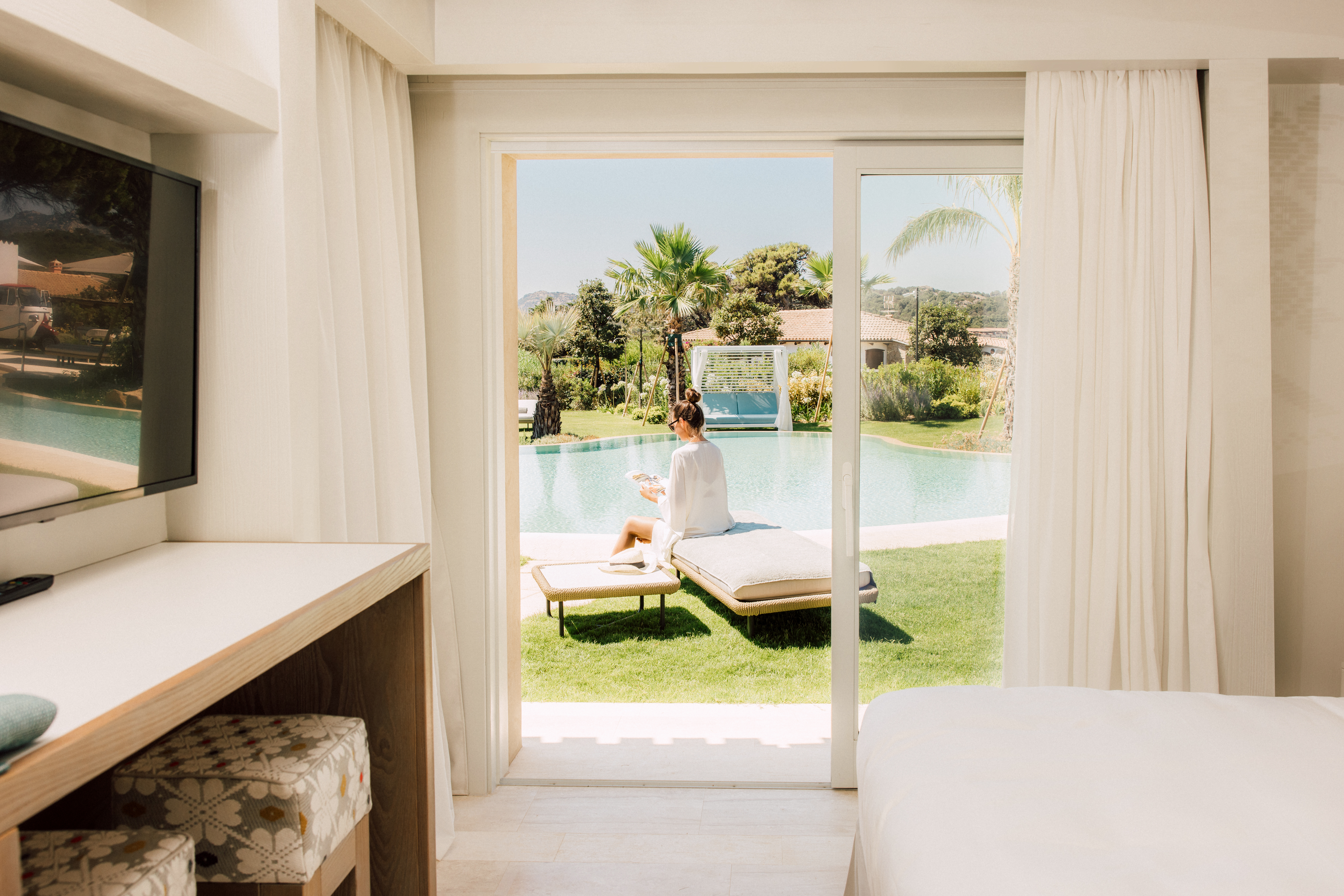 The view from inside a poolside suite featuring a woman sat on a lounger in the sun