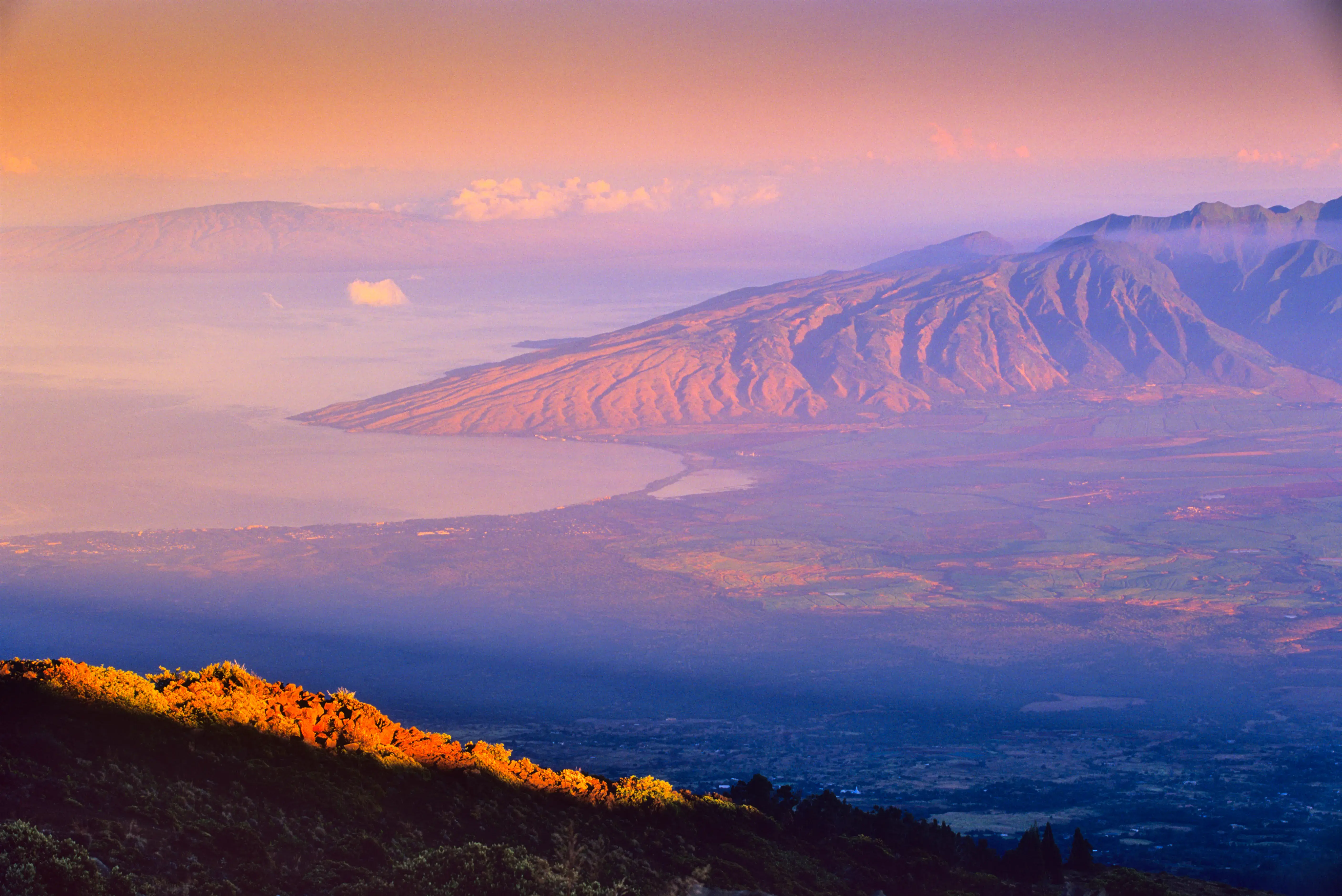 A hazy landscape of Maui at sunset cast in shades of pink and orange